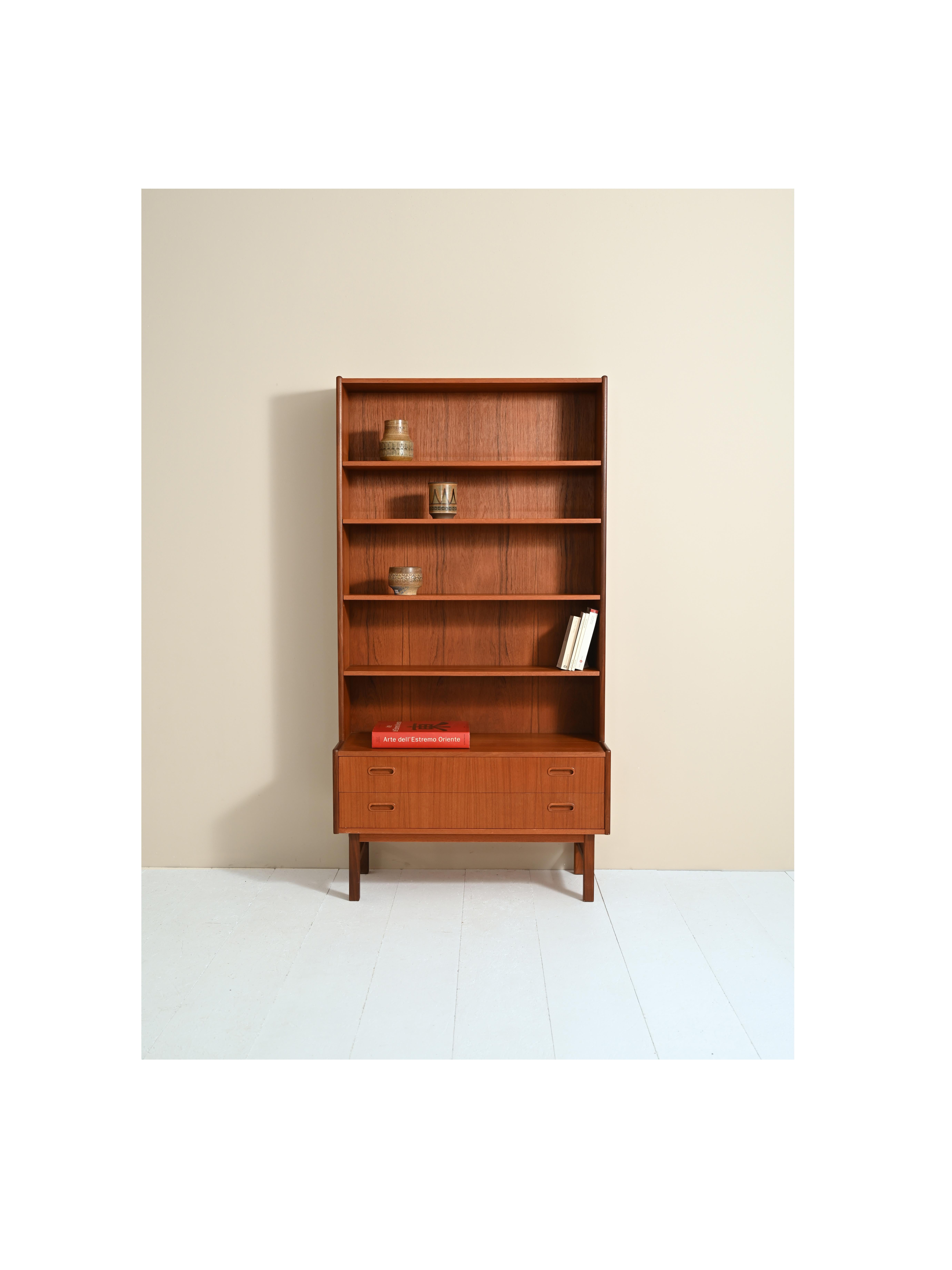 Original vintage teak cabinet of Scandinavian origin, consisting of two parts.
The upper part is a bookcase equipped with adjustable height shelves, the lower part is a cabinet equipped with two drawers and a compartment with a sliding door.
Ideal