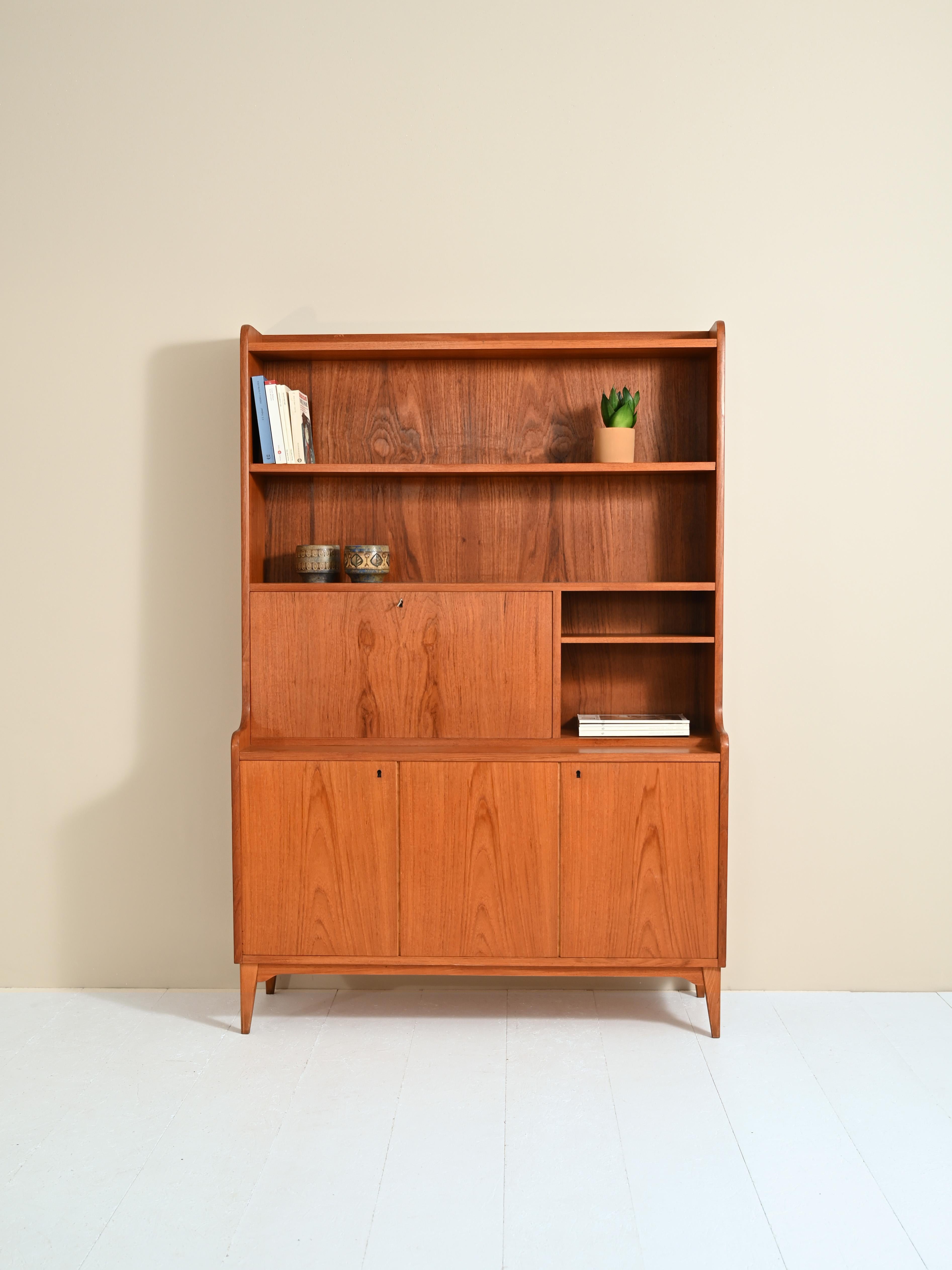 Original teak cabinet from the 1960s.
At the top there is shelving and a drop-down top that converts to a convenient writing desk when needed.
In the lower part the three hinged doors enclose a storage compartment equipped with a shelf on one side