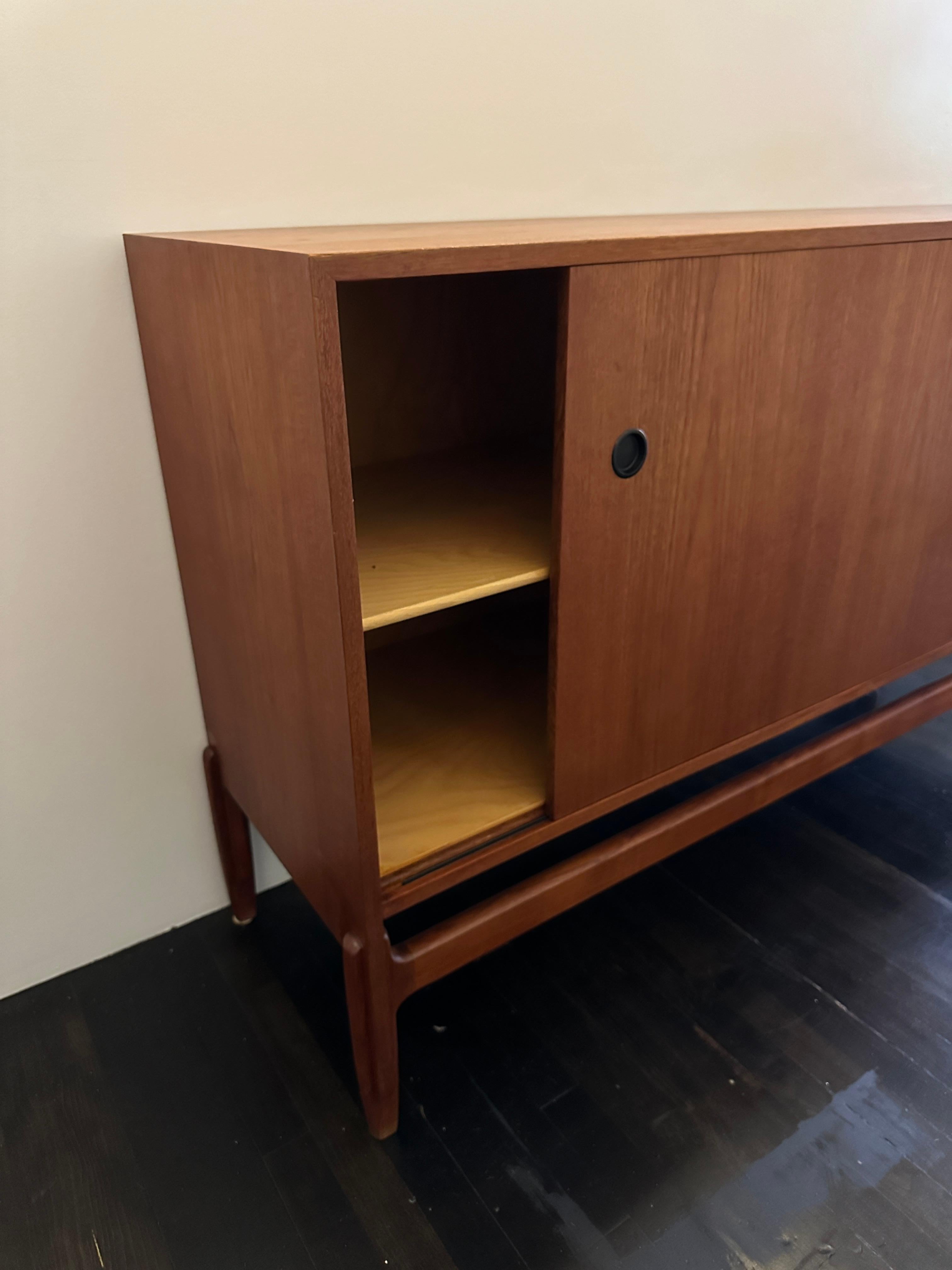 Teak credenza designed by Ejnar Larsen & Aksel Bender Madsen. Circa 1950s. Beautiful wood finish with black plastic drawer pulls. Sliding door on the left side with shelf interior and five drawers on the right side. 

Property from esteemed interior