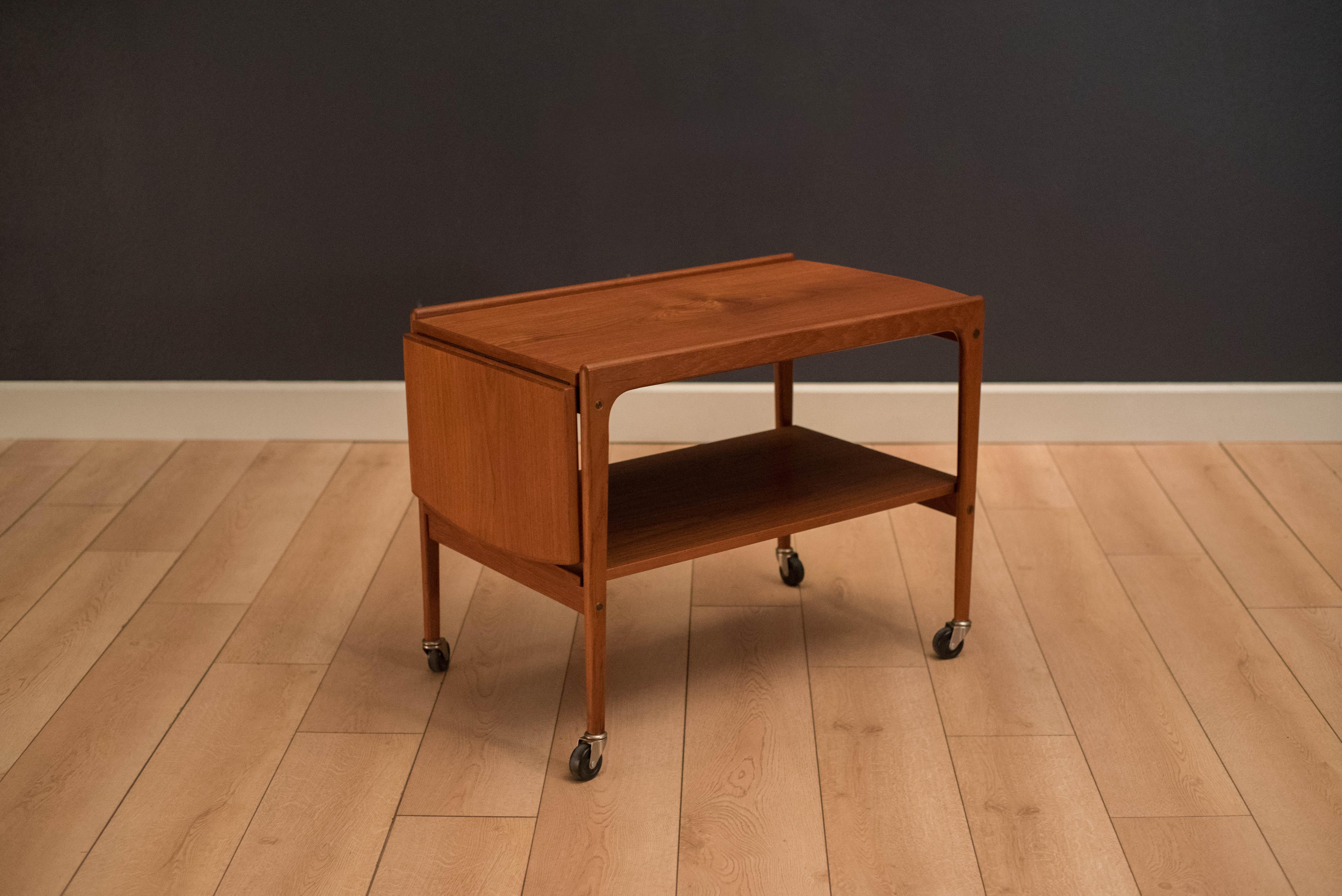 Mid-Century Modern tea cart or trolley in teak circa 1960s. This versatile piece is equipped with a drop leaf that slides to extend for a wider serving space. Features two tiers for extra storage display. 

Measures: Top extends 42.5