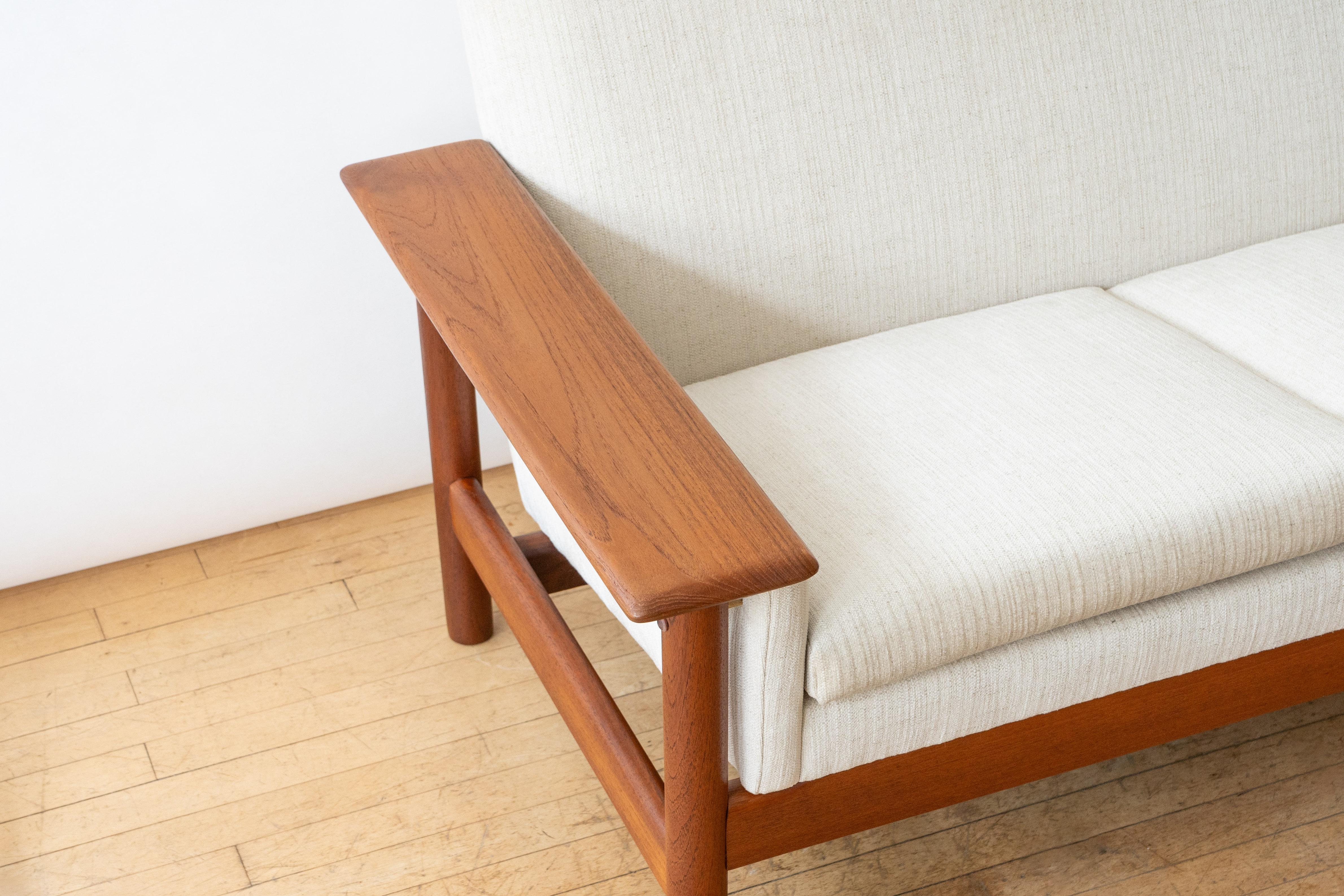 Norway, ca. 1960s. An attractive four-seat sofa attributed to Sven Ivar Dysthe for Dokka Möbler. Features heavy solid teak frame with wide paddle arms, upholstered back, and loose seat cushions . Cylindrical legs, brass mounting hardware, and new