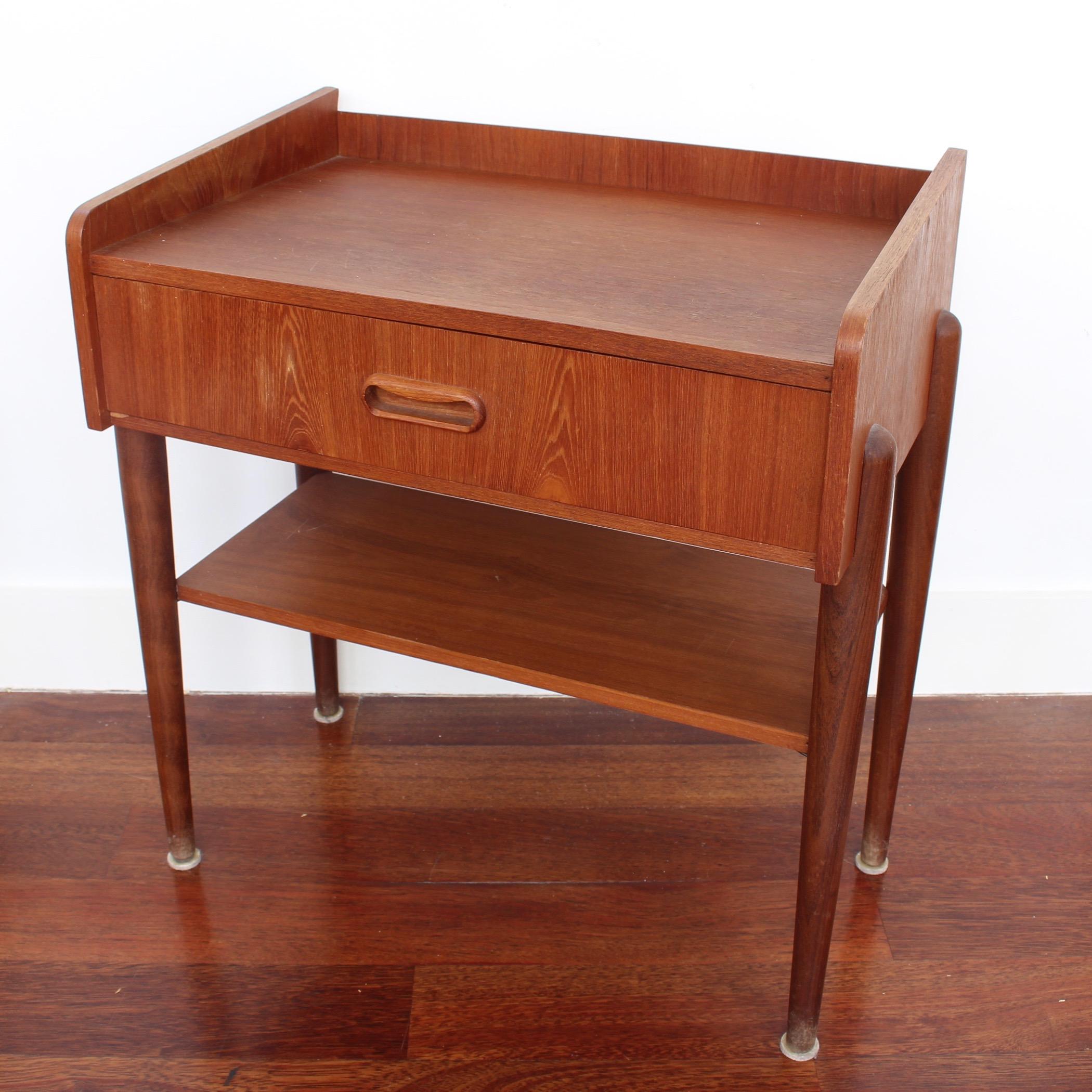 Scandinavian teak hallway table (circa 1960s). One drawer sits below the teak veneered top which sports a three-sided enclosure. Underneath, another horizontal surface for storage of books or magazines adds interest to the four-legged piece. It is