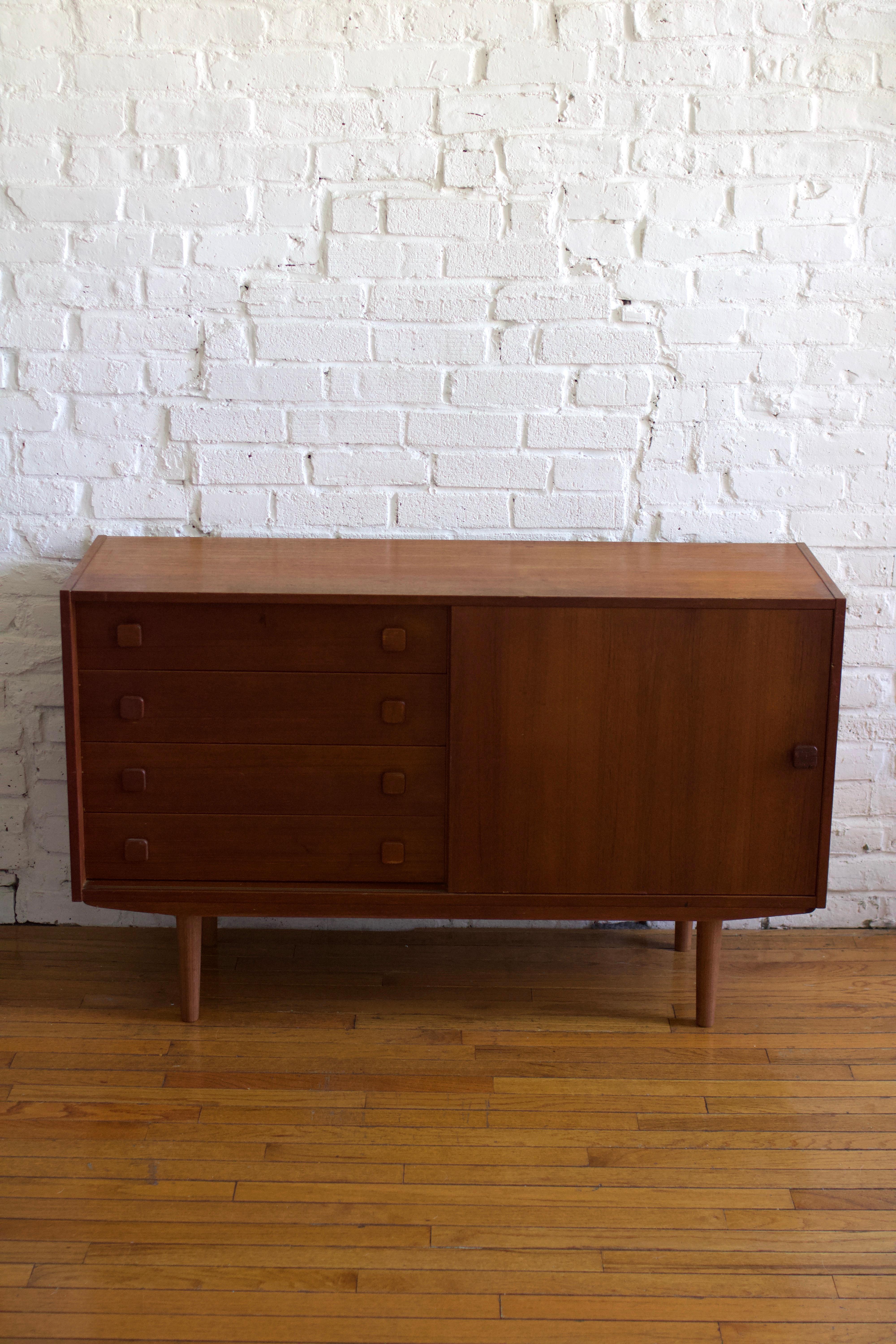 Attractive Scandinavian sideboard. This cabinet features a beautiful teak finish and four drawers with one sliding door. Perfect in a living room as a tv stand or in an entryway or  dining room as a storage piece.  

Based in Brooklyn - pick up or