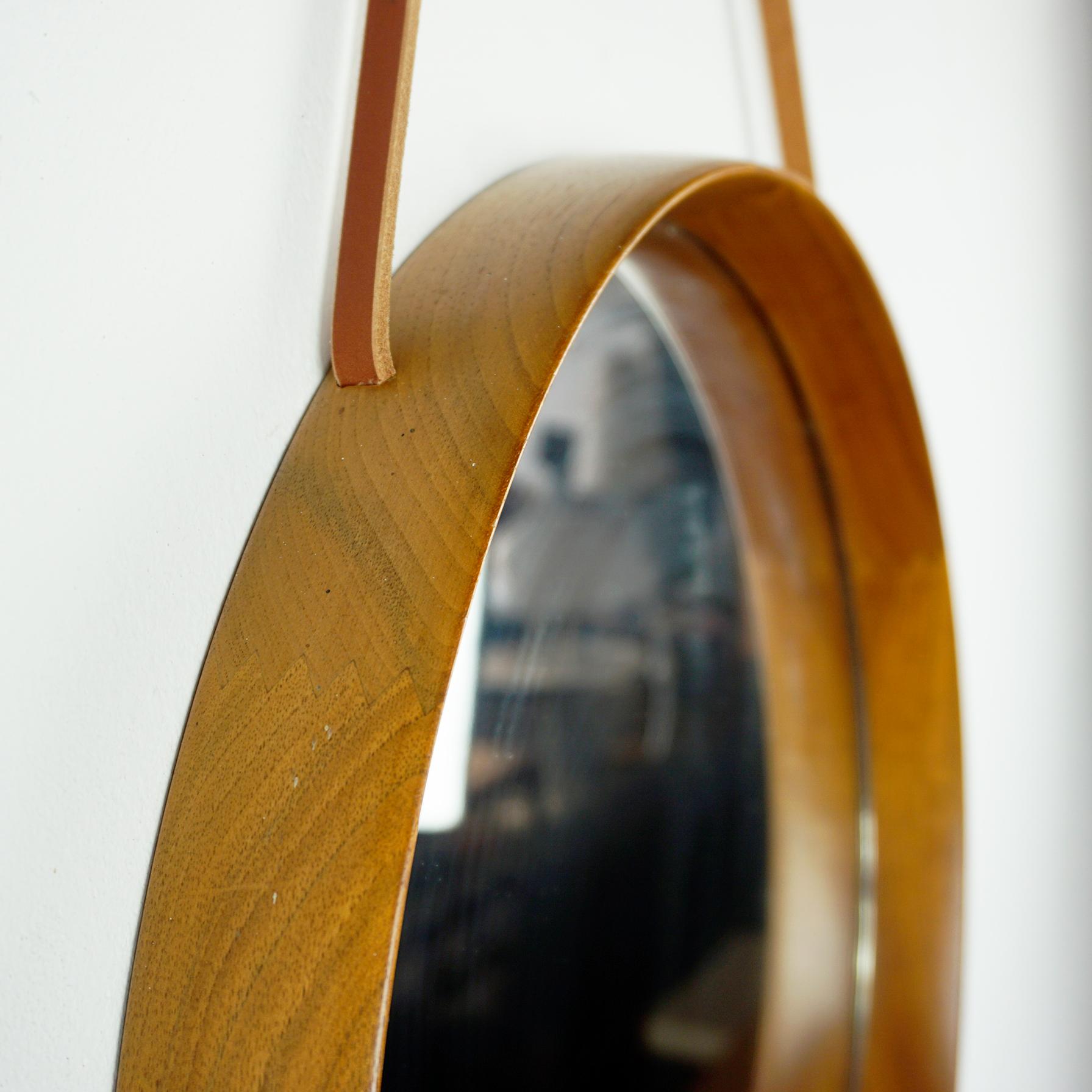   

This amazing Scandinavian Modern circular  teak wall mirror with leather hanging strap has been designed by Uno and Osten Kristiansson and manufactured by Luxus Vittsjö Sweden in the 1960s. 
 The frame circulates the glass and is made out of