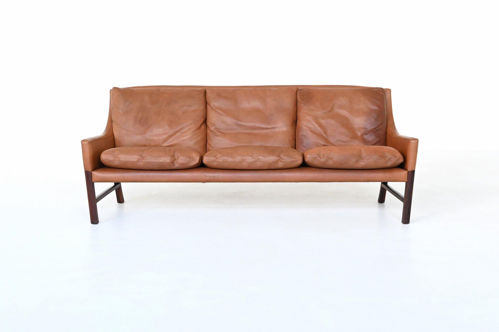 Questo elegante divano a tre posti è stato realizzato in Danimarca negli anni '60 e incarna il fascino senza tempo del design moderno scandinavo. Il divano è caratterizzato da una struttura elegante e scultorea in legno di palissandro massiccio, che