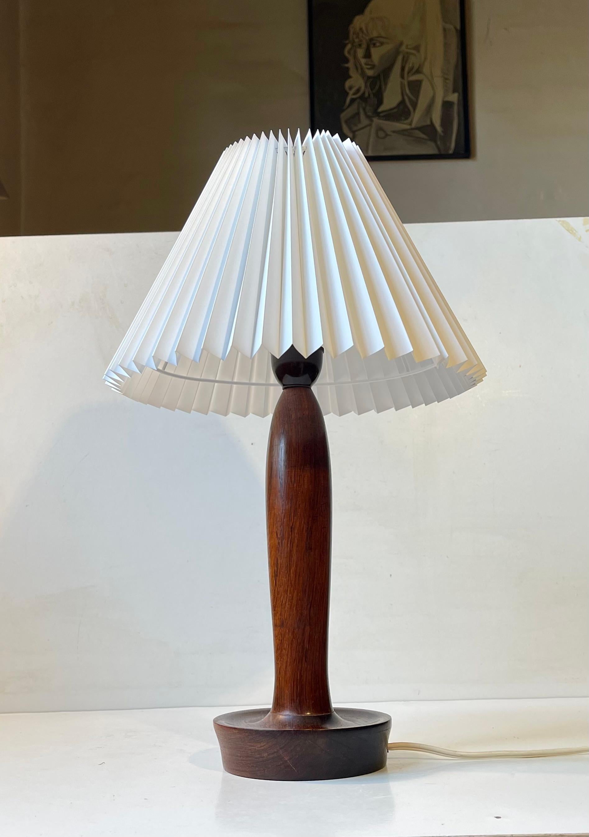 Organically shaped table lamp in engine turned solid rosewood. It features its original bakelit socket and showcases a new fluted white Danish shade in acrylic. It was made at Lyfa in Denmark circa 1960 in a style reminiscent of Bergboms and Alf