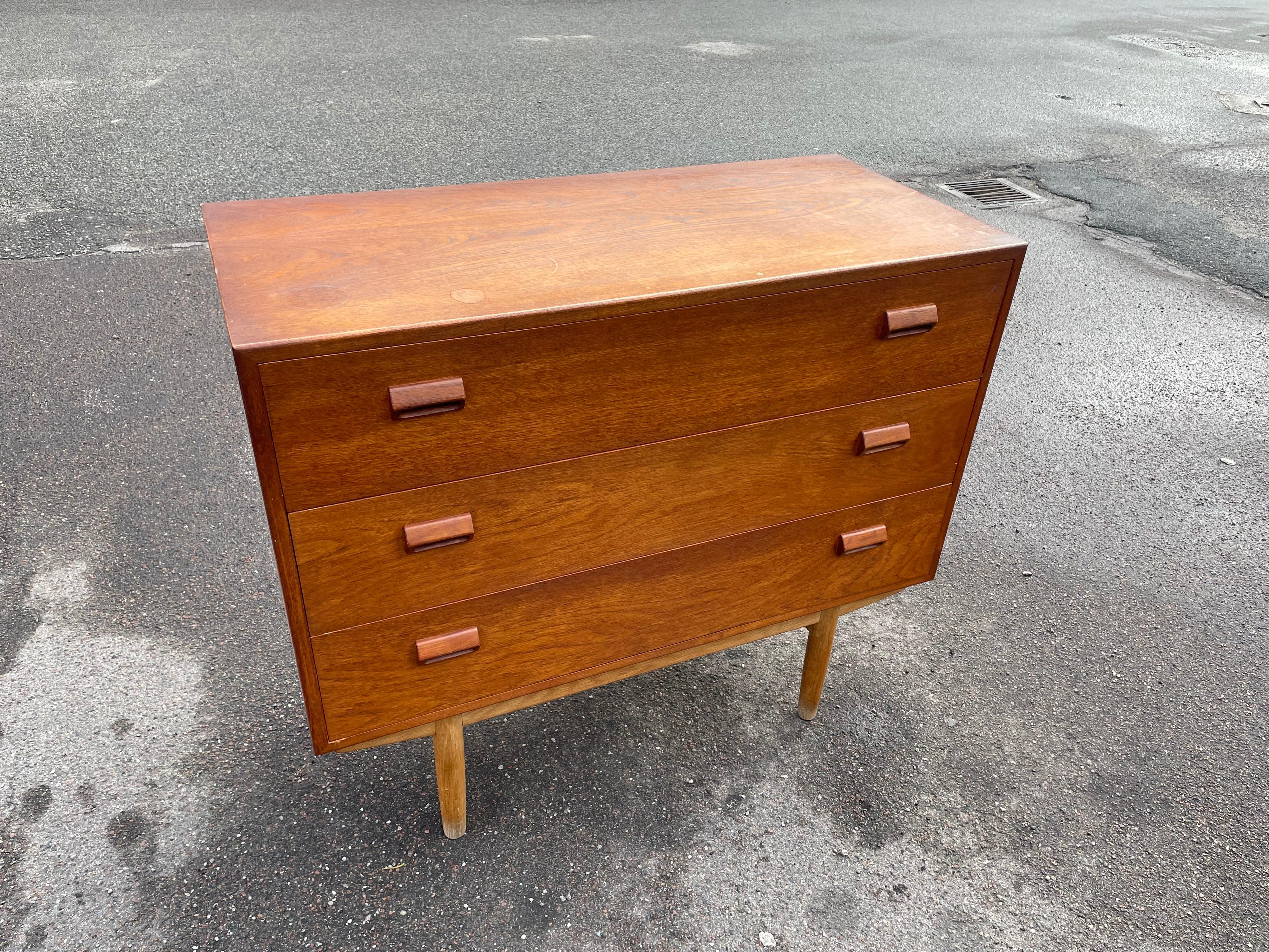 Midcentury teak vanity dresser designed by Borge Mogensen crafted of teak with three drawers, raised on oak legs. The face of the top drawer flips down, and pulls-out for a spacious writing surface revealing a series of small drawers and a hidden