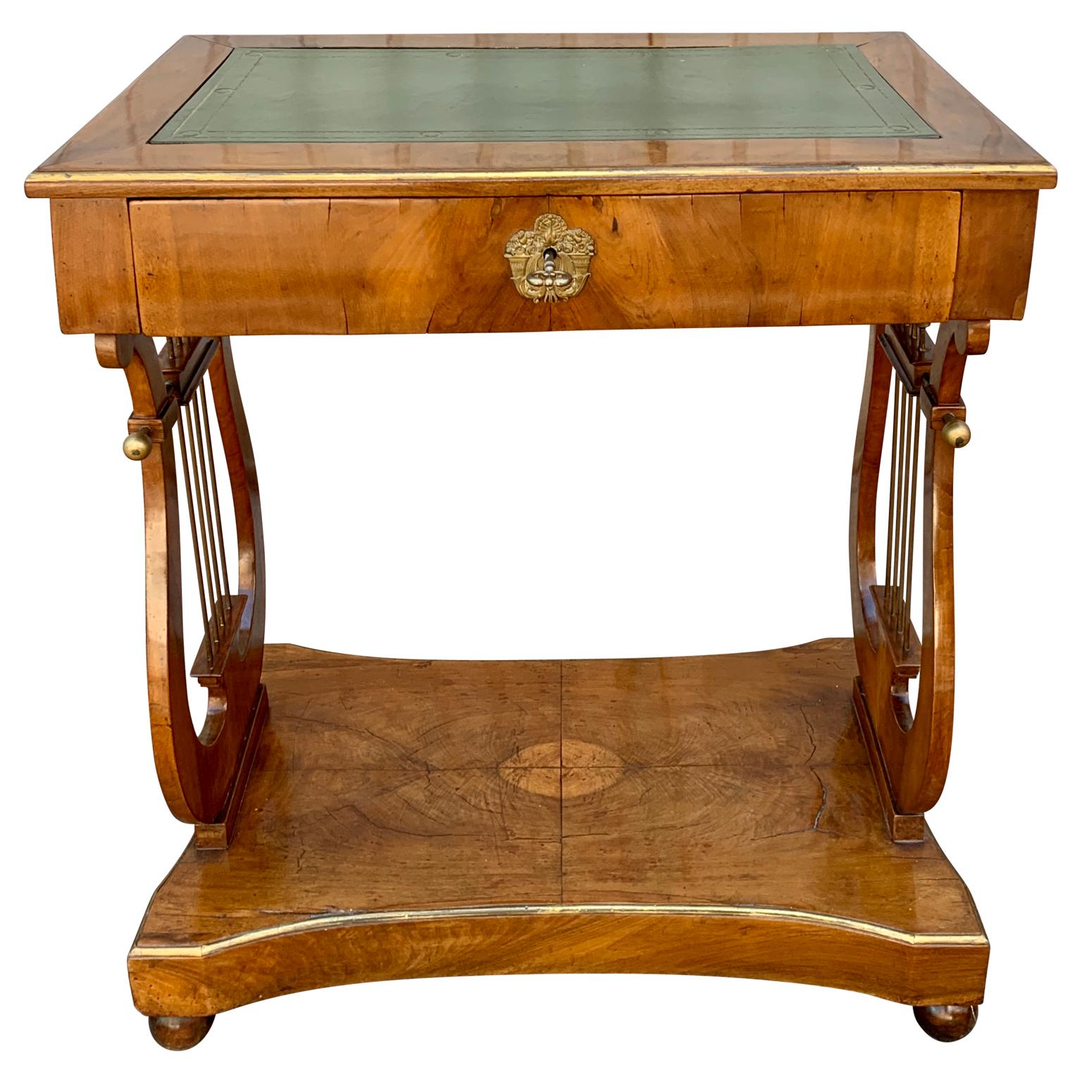 A small mahogany and walnut veneered table or writing desk with brass holders in the lyres formed sides. The top is provided with inlaid green leather; the drawers have divided small compartments. The small table has brass lists decorating all