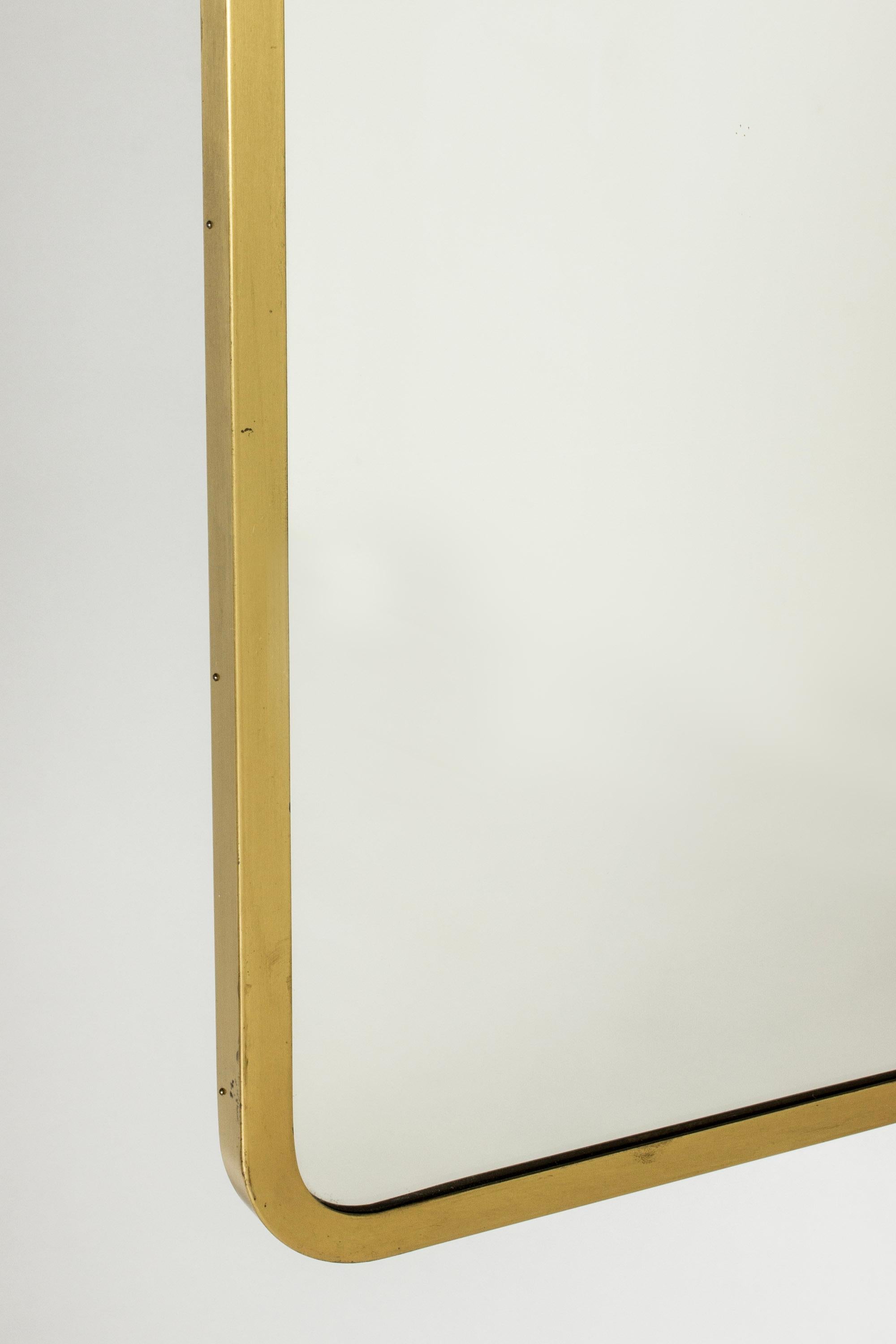 Großer, eleganter Wandspiegel von Ystad-Metall mit einem Messingrahmen mit abgerundeten Ecken. Dekorative Schleife auf der Oberseite.