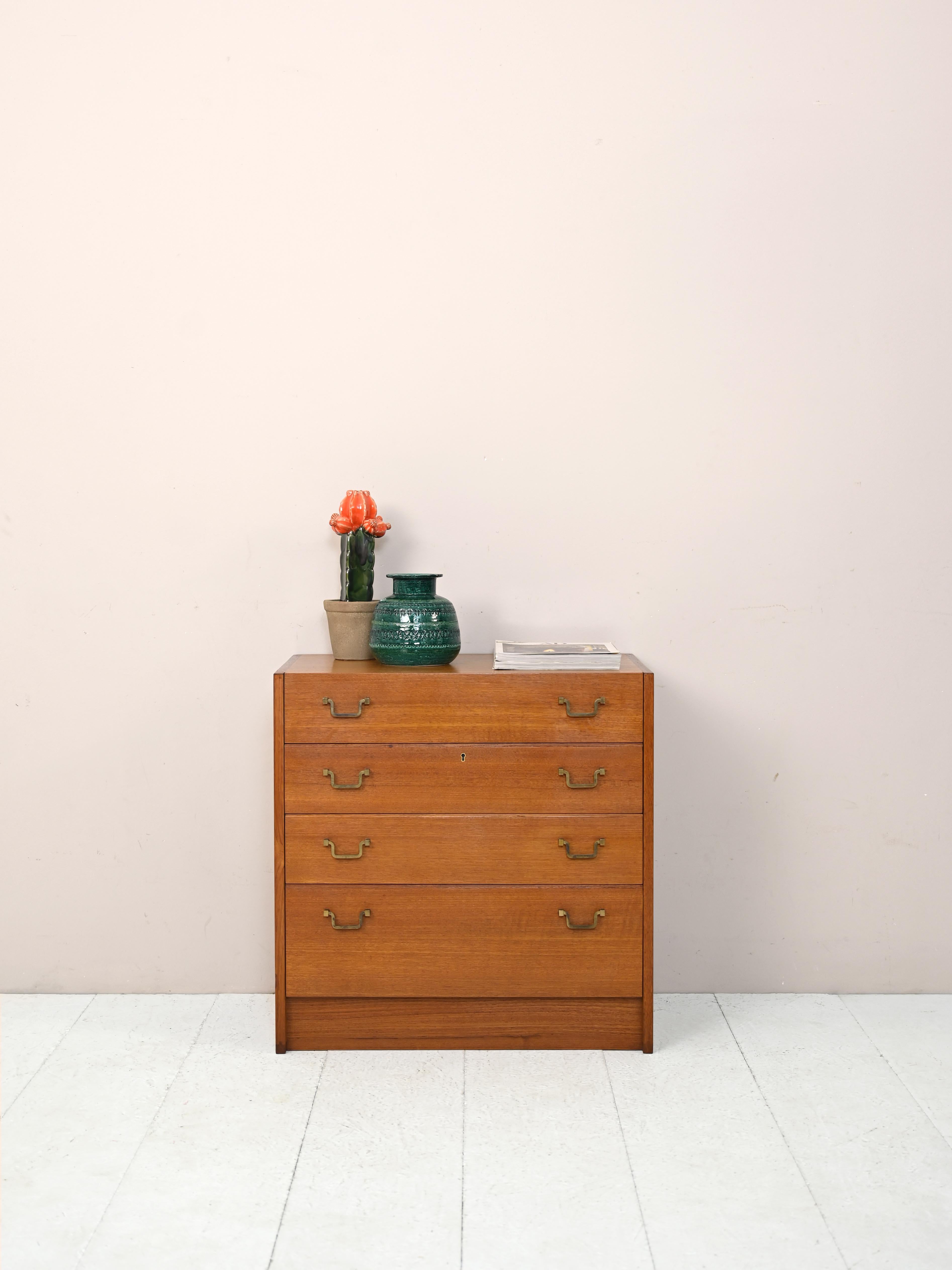 1960s teak cabinet with 4 drawers.

This chest of drawers is distinguished by the shape of the base that rests directly on the floor without the presence of legs. The linear structure and golden handles on the drawers make it a modern and elegant