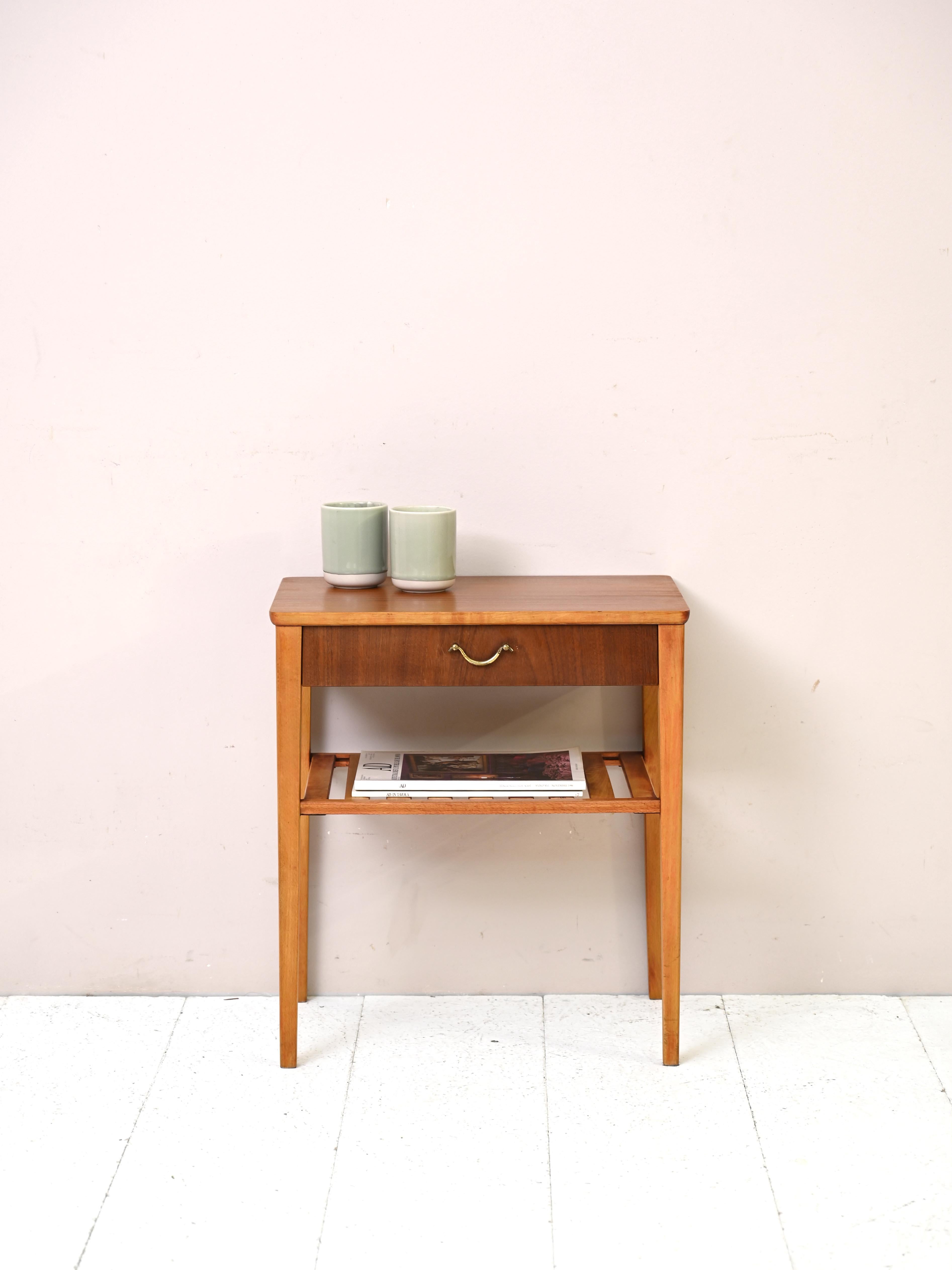 Teak and birch bedside table with golden handle.

An original piece of furniture from the 1960s in perfect retro style.
The top is teak as is the drawer. The legs and magazine rack top, on the other hand, are made of birch. The use of the two