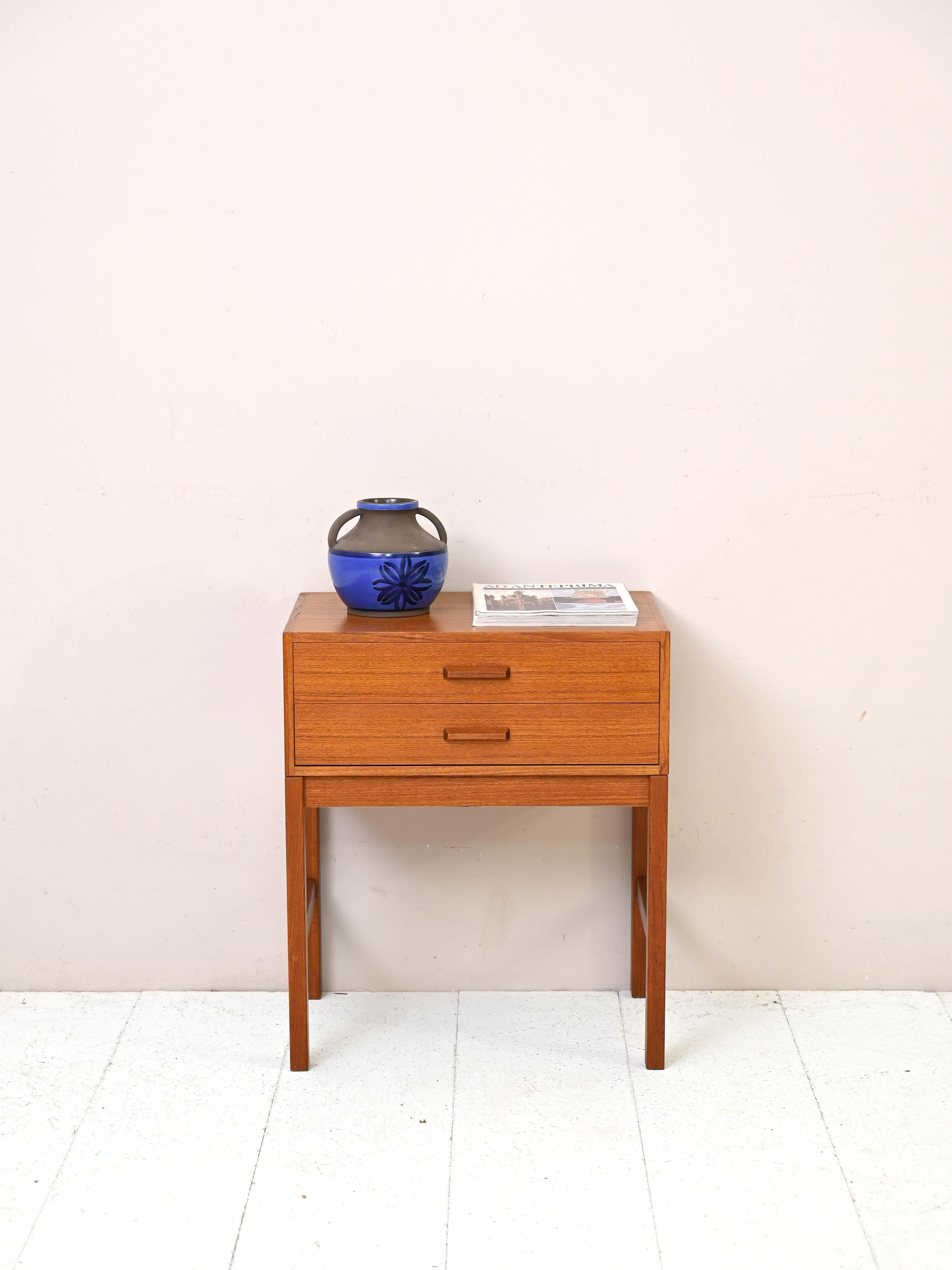 Table de chevet en teck des années 1960.

Ce meuble vintage présente des formes simples et carrées et un cadre entièrement en teck. La poignée des deux tiroirs est également en bois sculpté.
Idéal comme table de nuit mais aussi comme meuble