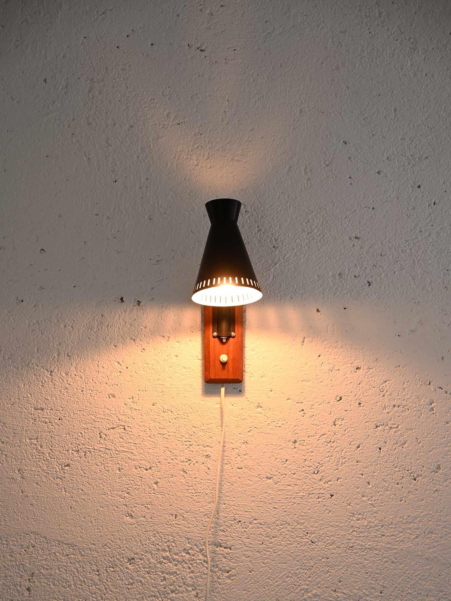 1960s wall lamp.

Particular wall sconce consisting of the black-painted sheet metal shade and a brass arm supported by the teak base that conceals the electrical part.
A lamp with a vintage flavor that can be used to characterize the bedroom,