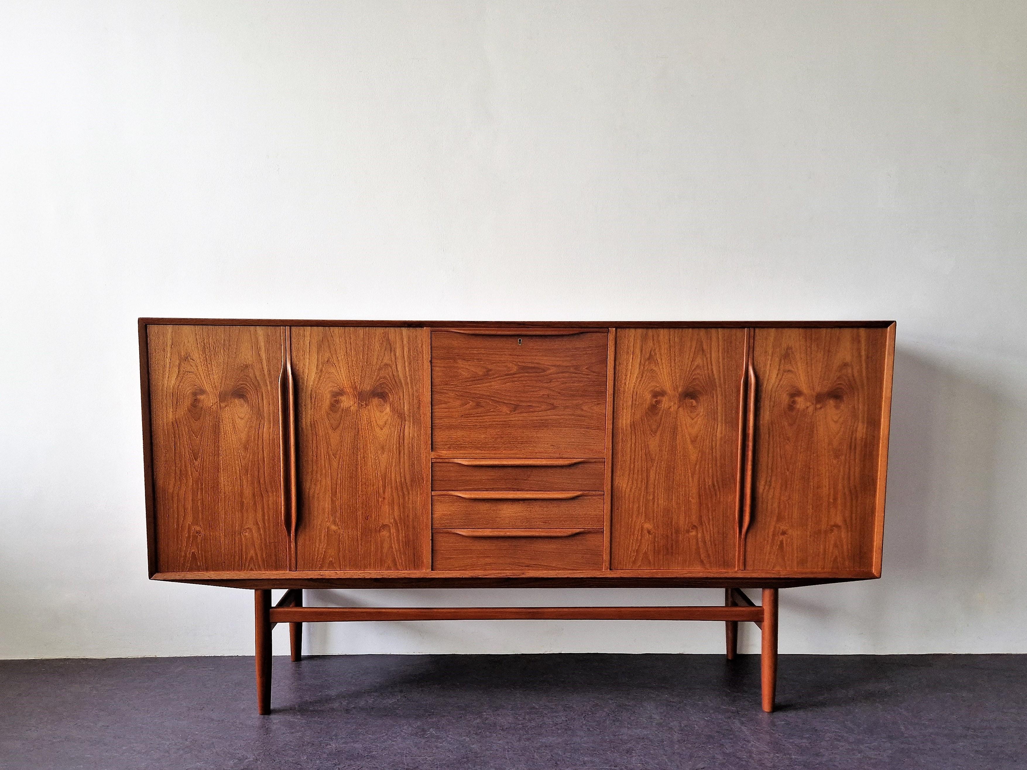 This beautiful vintage teak veneer highboard was imported from Denmark. It has 2 doors on both sides with 2  shelves each. In the middle a drop front mirrored cabinet (nice to set up as a bar), that has a round shaped black wooden removable shelf, a