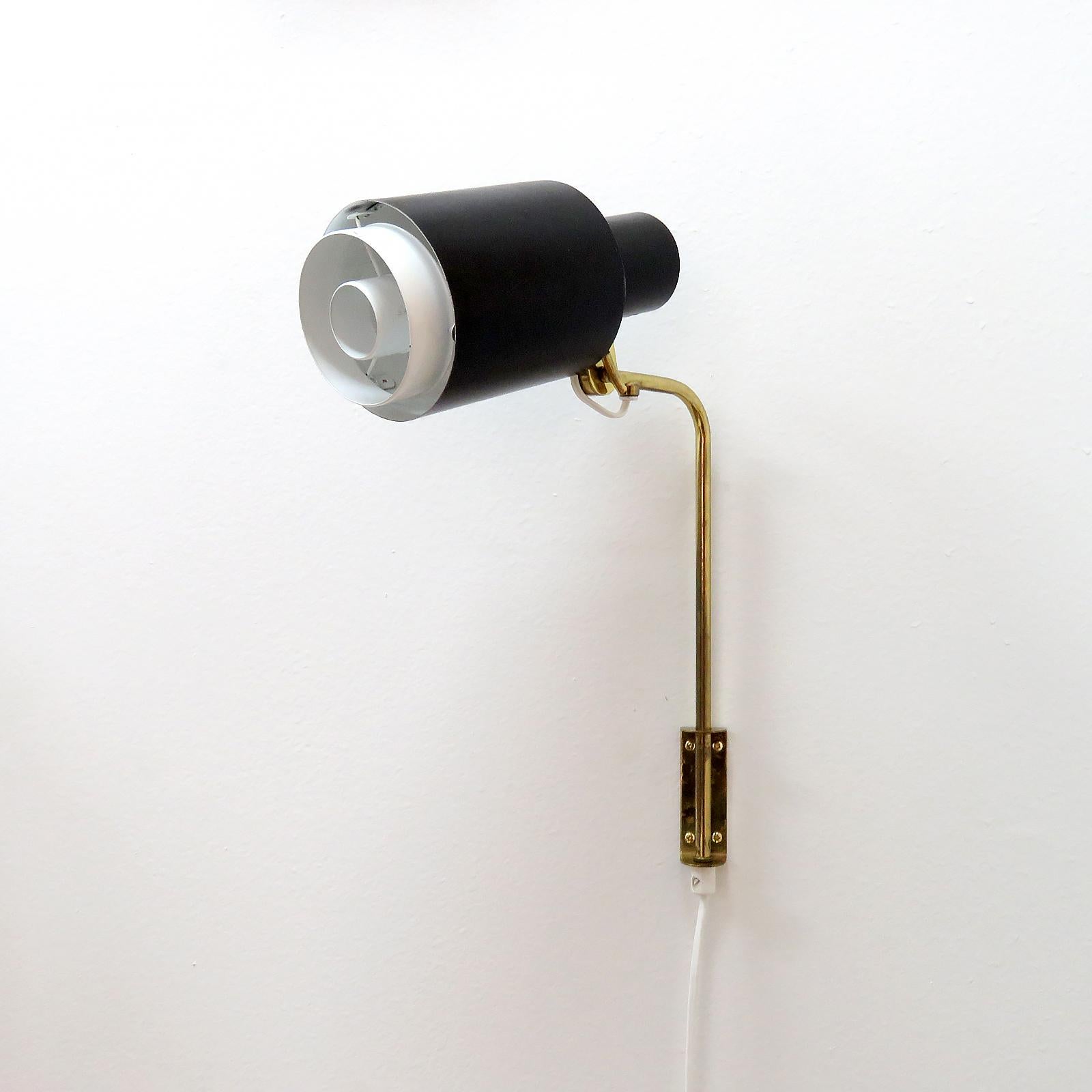 Elegant articulate plug-in wall light by Itsu, Finland, 1960s, black double-tier body with white detachable diffusor at the bottom edge, mounted on an L-shape brass arm with swivel joint at the shade, arm can move to either side, white cord with