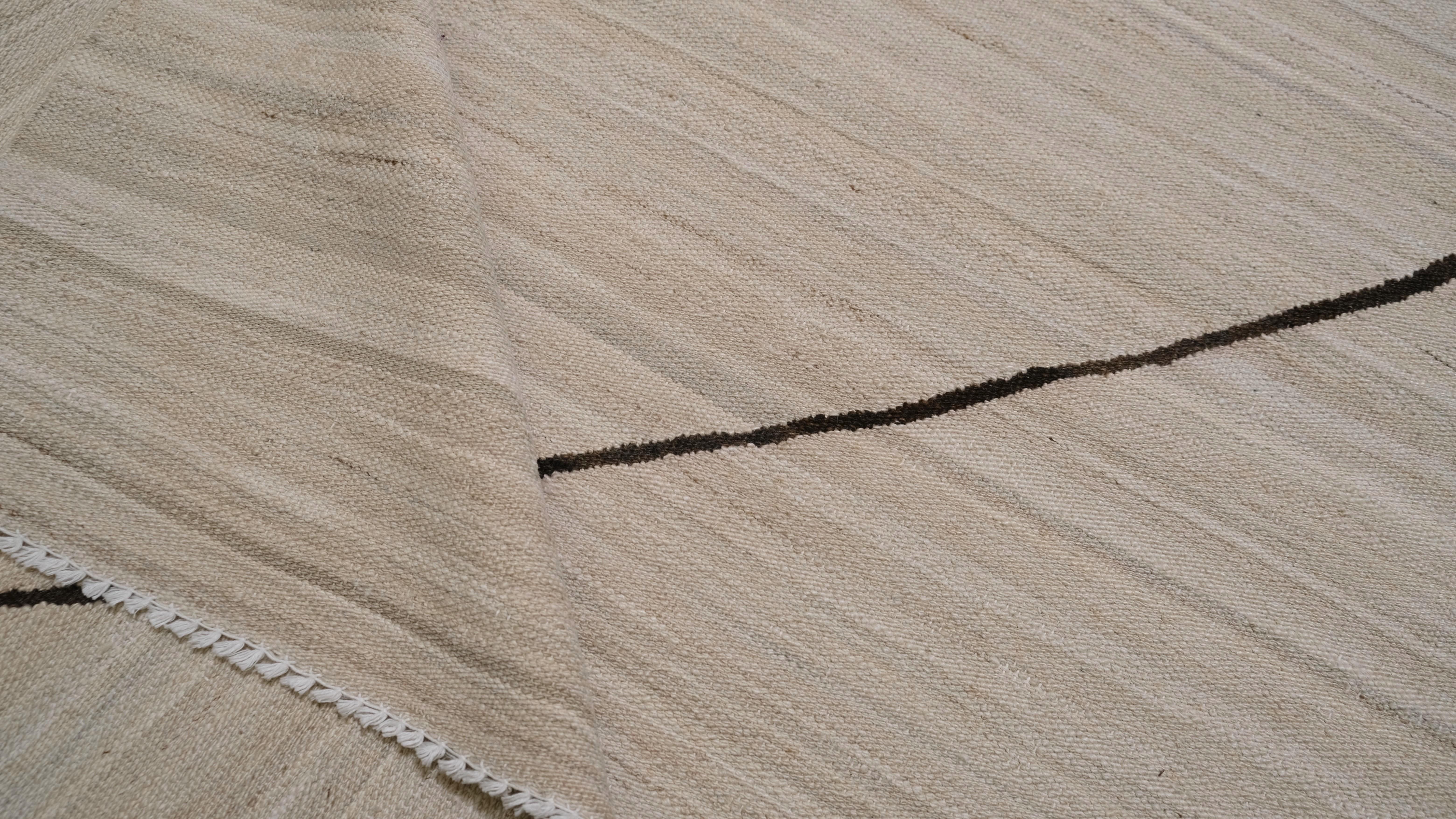 Ce tapis minimaliste en laine tissée à la main allie sans effort simplicité et élégance moderne. Avec un fond beige doux entrecoupé de lignes brunes abstraites, ce design évoque un sentiment de sophistication et de charme discret. Son esthétique