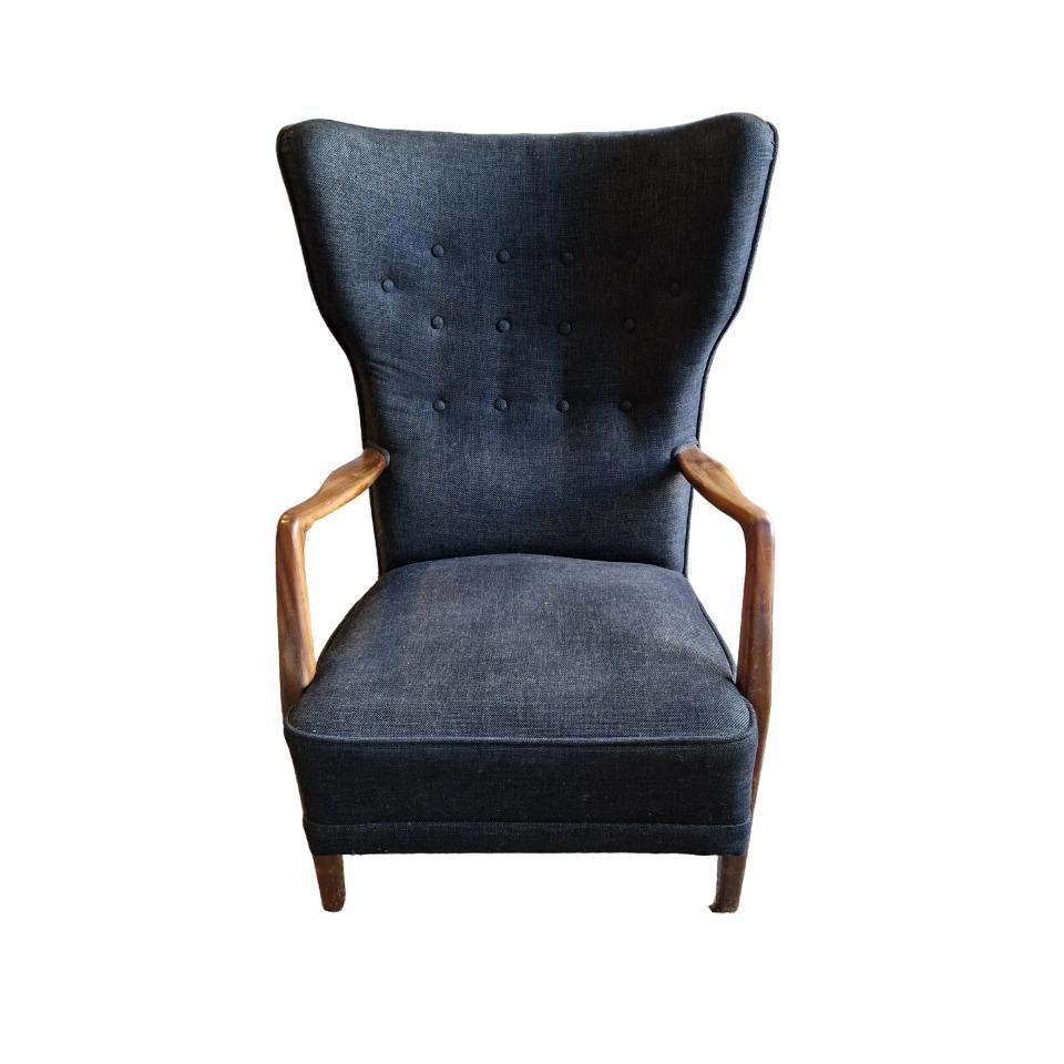 Imposing armchair with a blue Fabric. The back has a winged shape and the seating is thick for maximum comfort. The wooden armrests have an organic shape, typical of the scandinavian look.