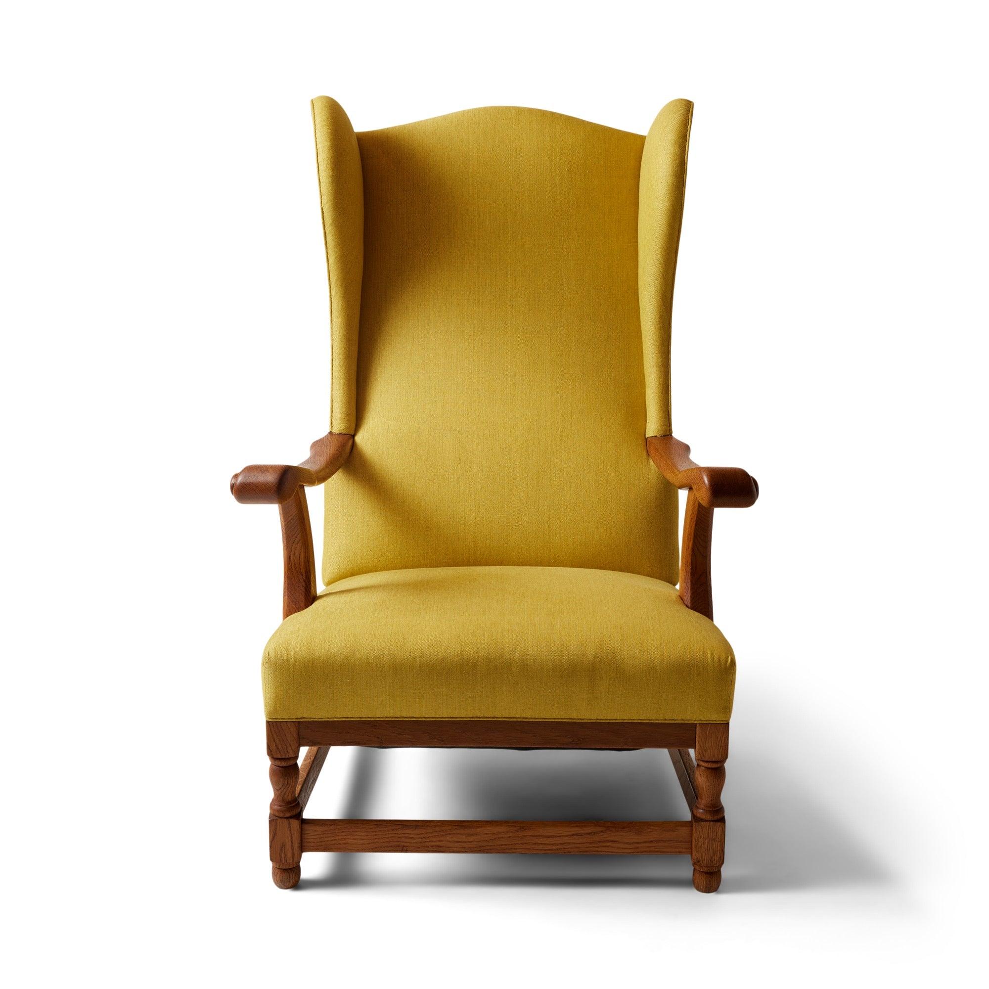 Fauteuil à oreilles rembourré avec des accoudoirs sculptés et un cadre en bois de chêne apparent.