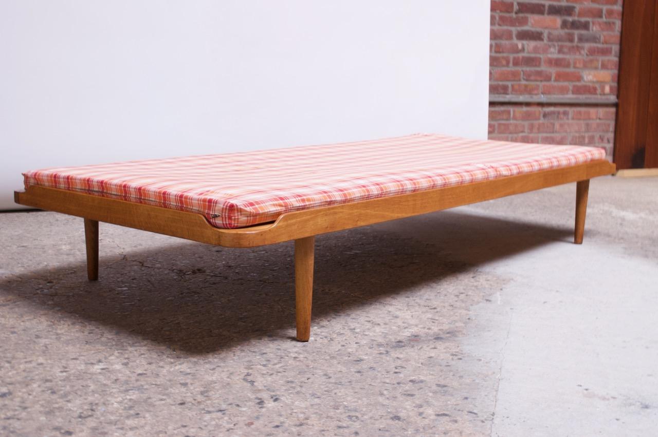 Circa 1960s Danish daybed in solid oak with a plaid cushion in white, orange, and red (vintage, although likely not original). Modest form with slat construction supported by oak tapered legs.
Cushion is thinned out from use and could benefit from