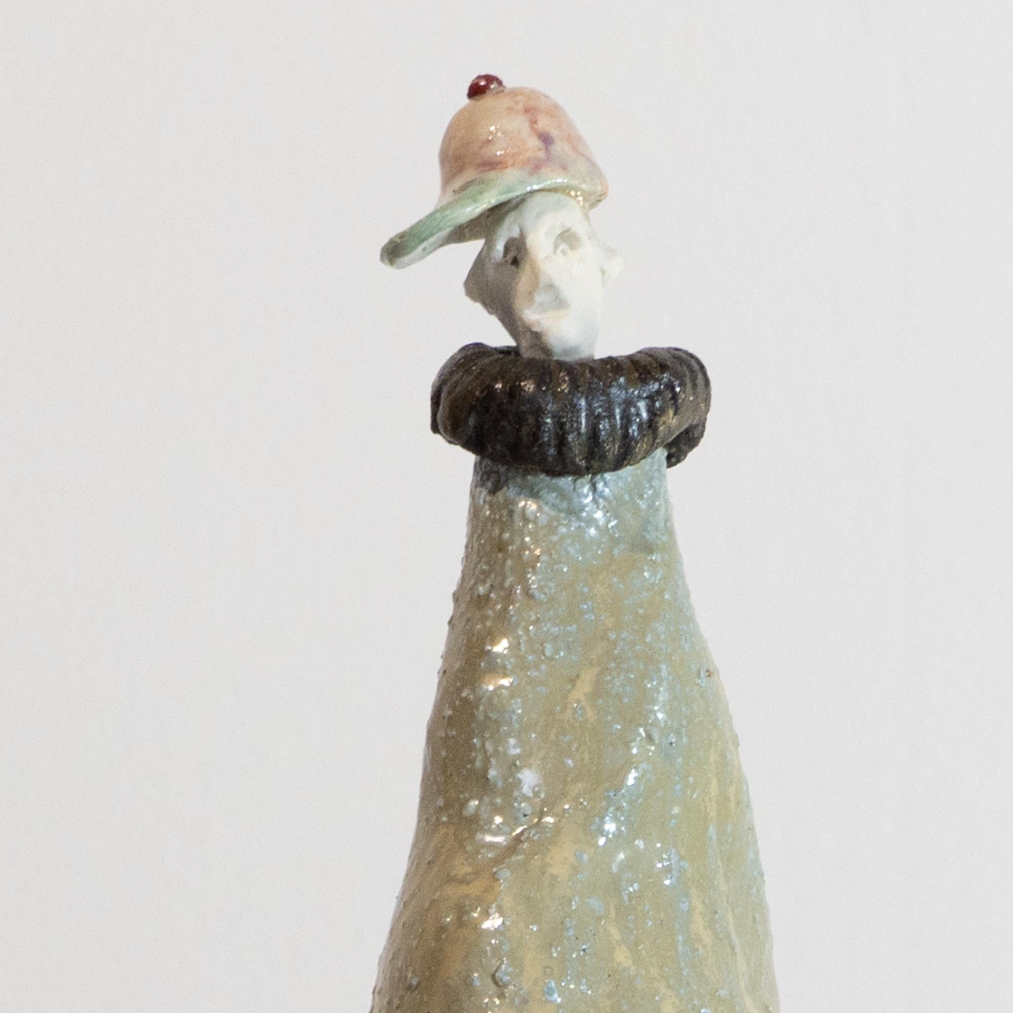 “Baseball Cap Extravagant” is a high-fired stoneware sculpture from Óscar Aldonza Torres’s “The Extravagants” series, finished in pale olive and sandy glazes that pool organically over its tapered, tripod base. A pastel-pink baseball cap and
