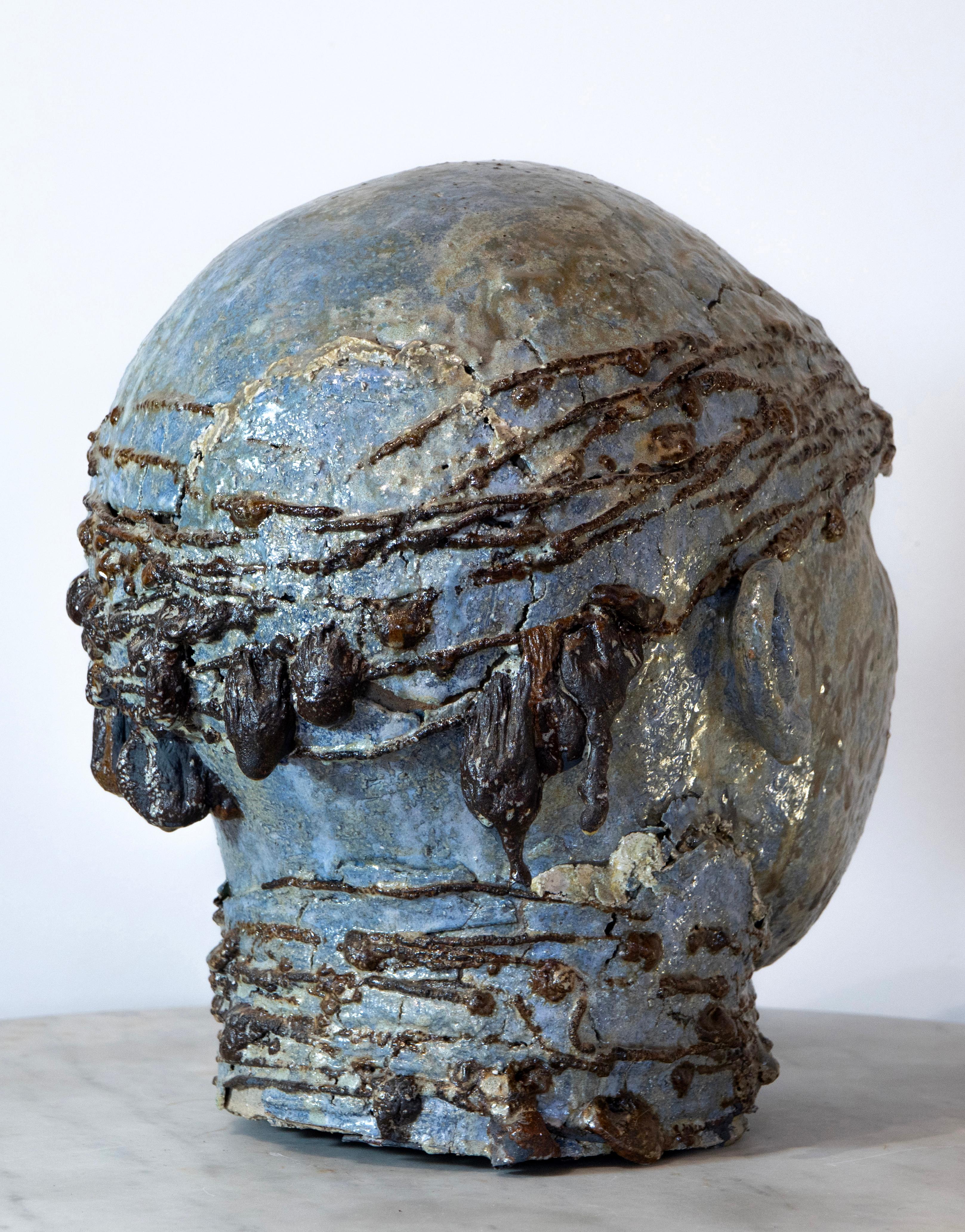 La escultura de hierro y refractario esmaltado a alta temperatura evoca la tierra y el mar mediterráneos a través de capas de tonos verde azulados y texturas táctiles. Cabeza de Aldonza con pañuelo (38 × 36 × 29,5 cm) es una obra icónica que