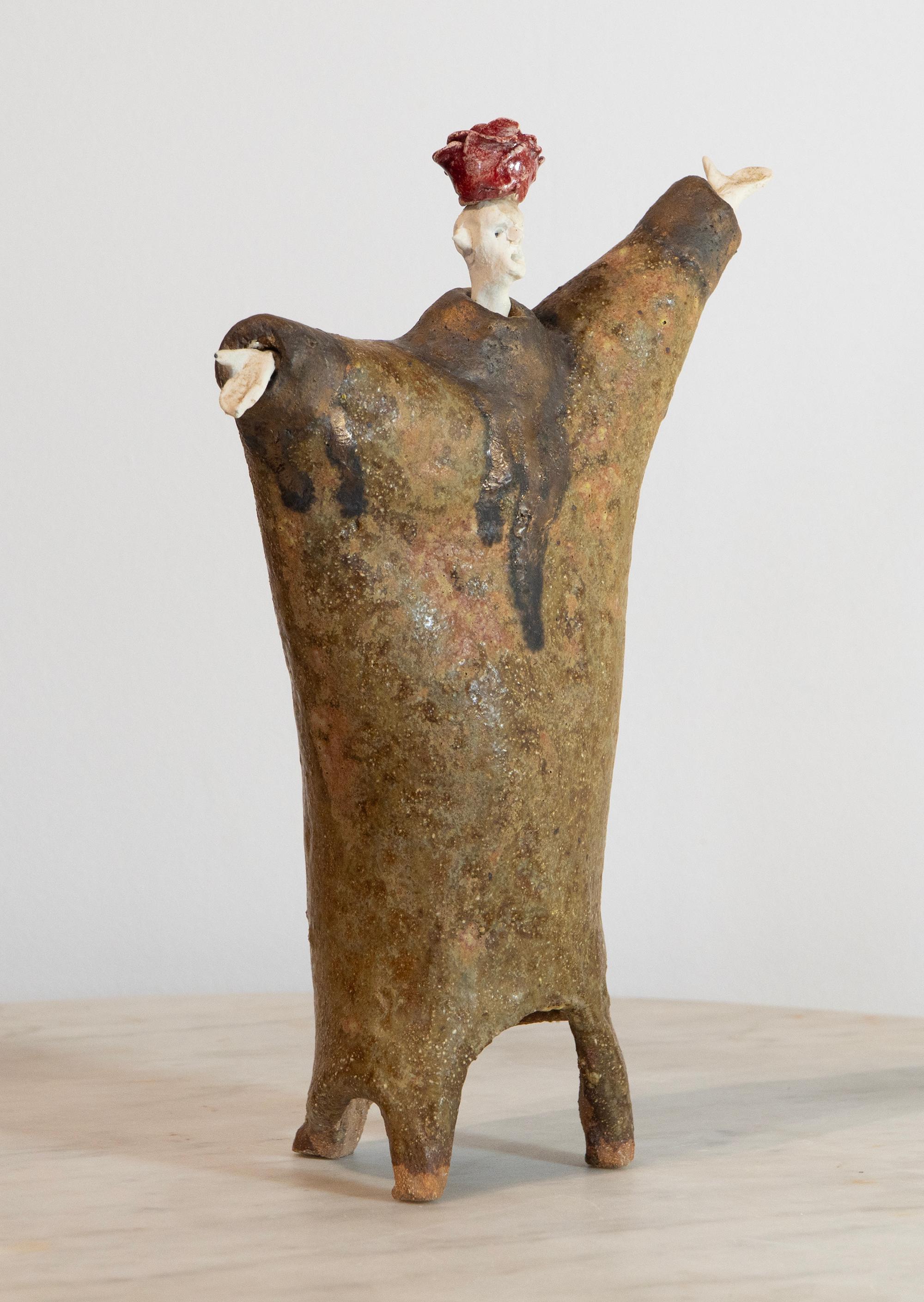 “Rosebud-Hat Extravagant” belongs to Óscar Aldonza Torres’s “The Extravagants” series: a high-fired stoneware sculpture topped by a scarlet, petal-like hat that evokes a rosebud. The figure’s affable stance—with outstretched arms and an