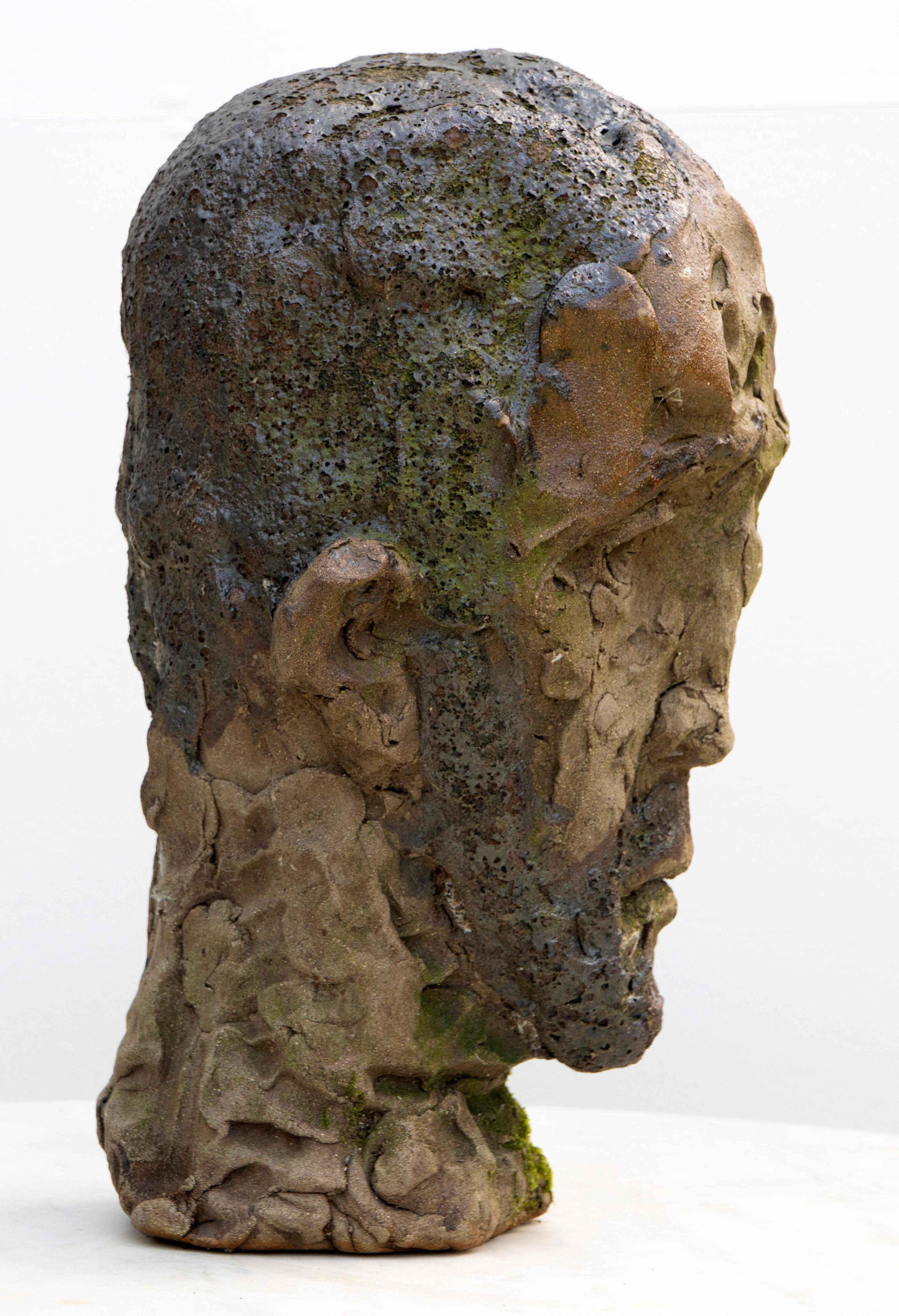 Dieser Kopf aus Moos-Patina-Steinzeug zeigt raue Raku-Texturen und unvorhersehbare Glasureffekte in einer beeindruckenden Keramikskulptur. Die in gedämpften Grautönen, erdigen Grüntönen und zartem Taupe marmorierte Oberfläche des Steingutkopfes