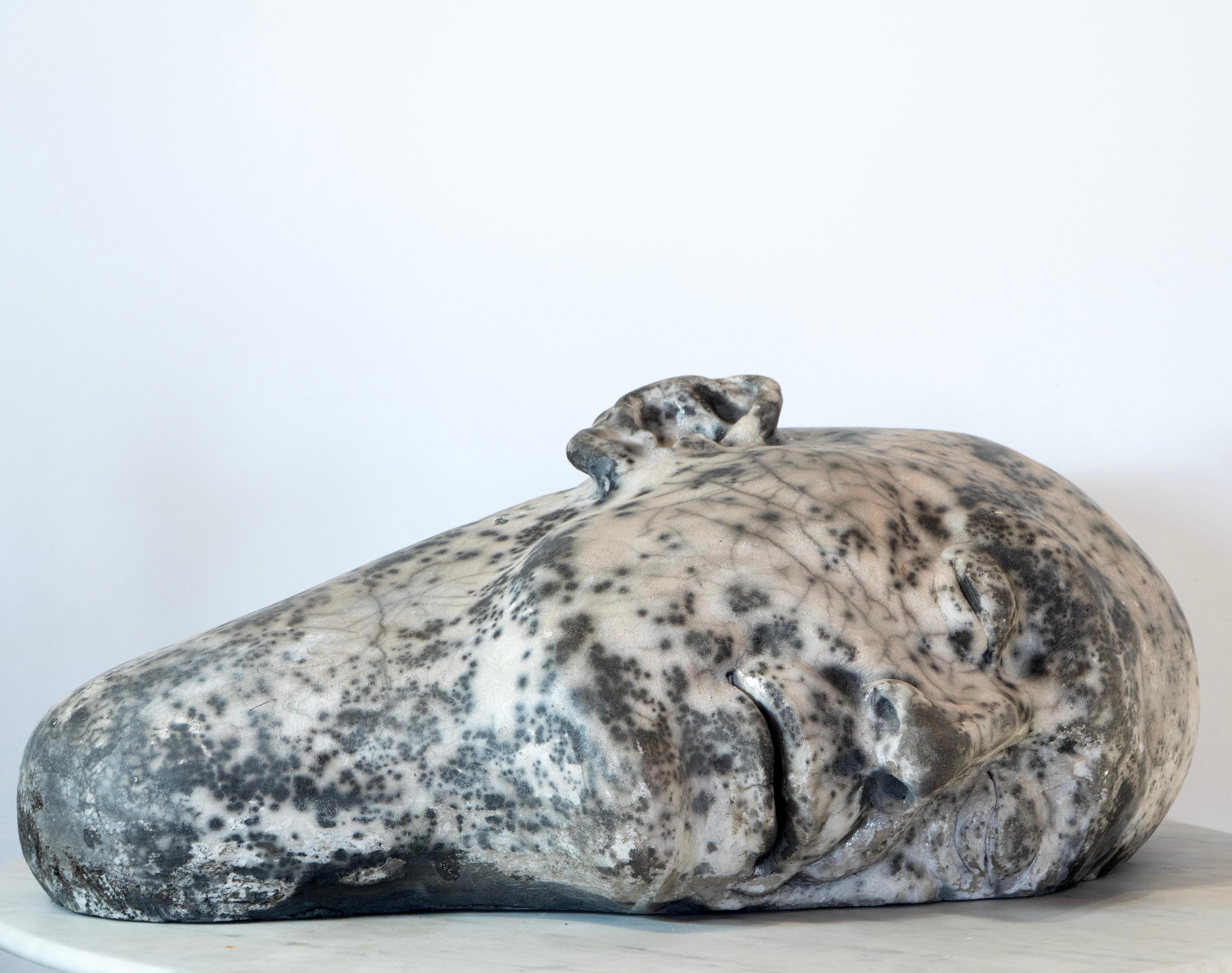 La sculpture de tête en céramique Raku blanche présente des textures organiques de craquelures de terre et une forme méditative, faisant le lien entre la terre, le rituel et l'introspection. Reclining Head (28 × 47 × 62 cm) d'Aldonza est réalisée en