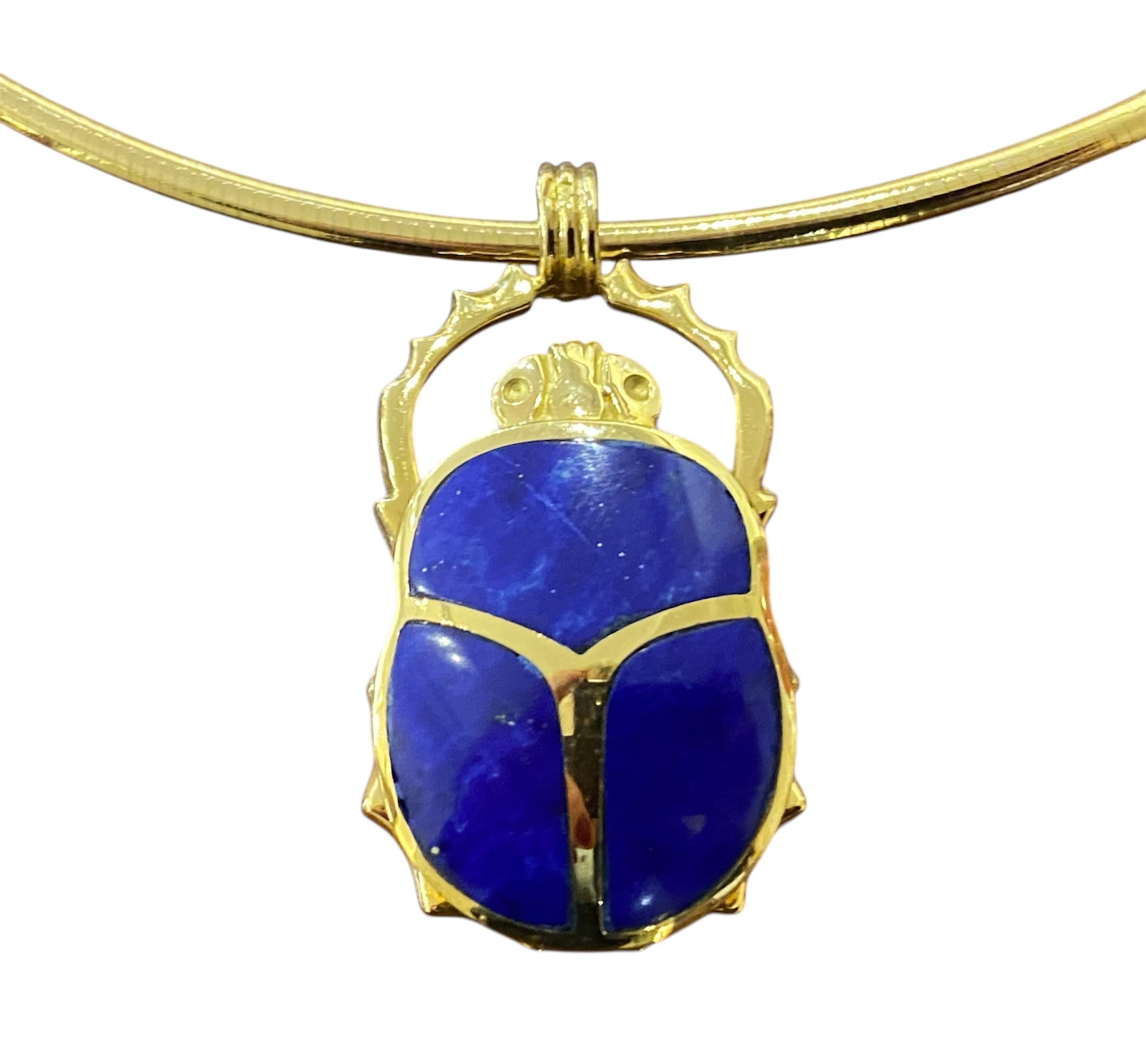 Girocollo con maglia semirigida in oro giallo 18kt - 750‰, con un pendente a forma di scarabeo ornato da tre pietre di lapislazzuli blu intenso e profondo. Lo scarabeo, ispirato al simbolismo dell'Antico Egitto, rappresenta il rinnovamento, la