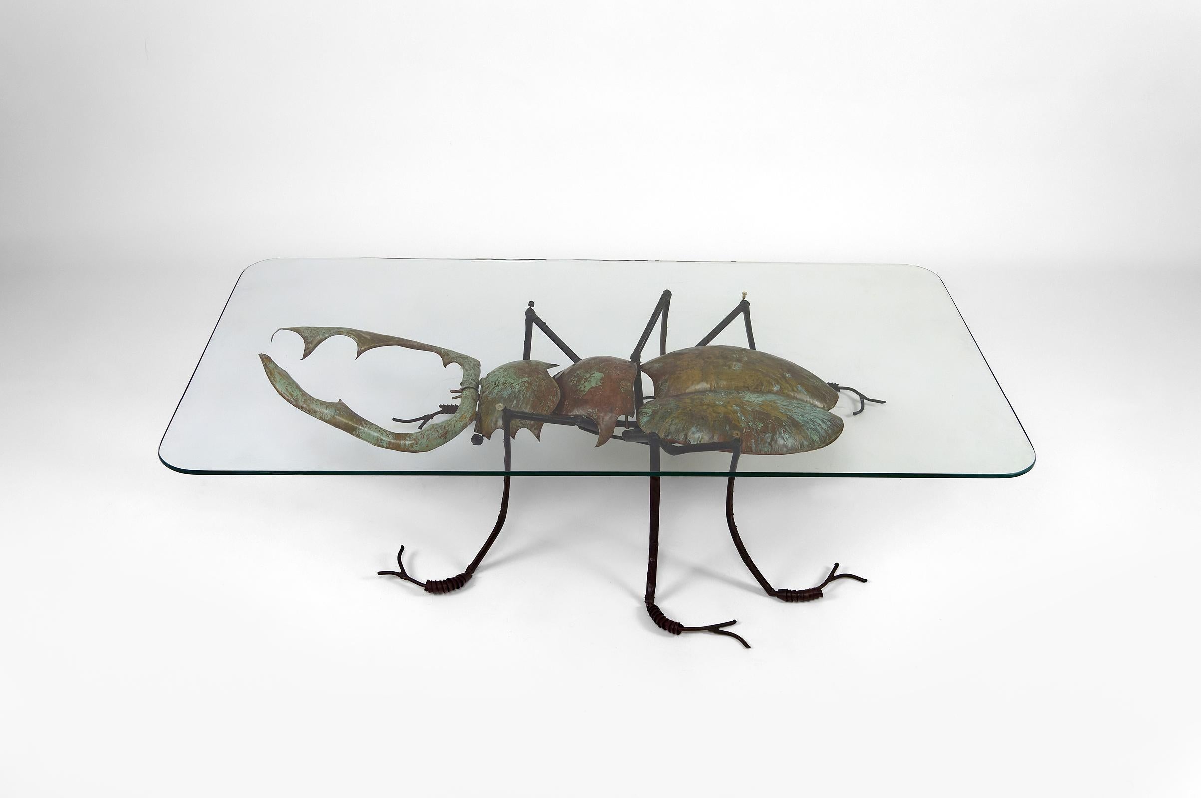 Superb coffee table composed of a metal sculpture and a glass top.

The metal sculpture represents a stag beetle / scarab in wrought iron, patinated brass and other various metals. The insect is covered in a verdigris / rust patina.
The top is a