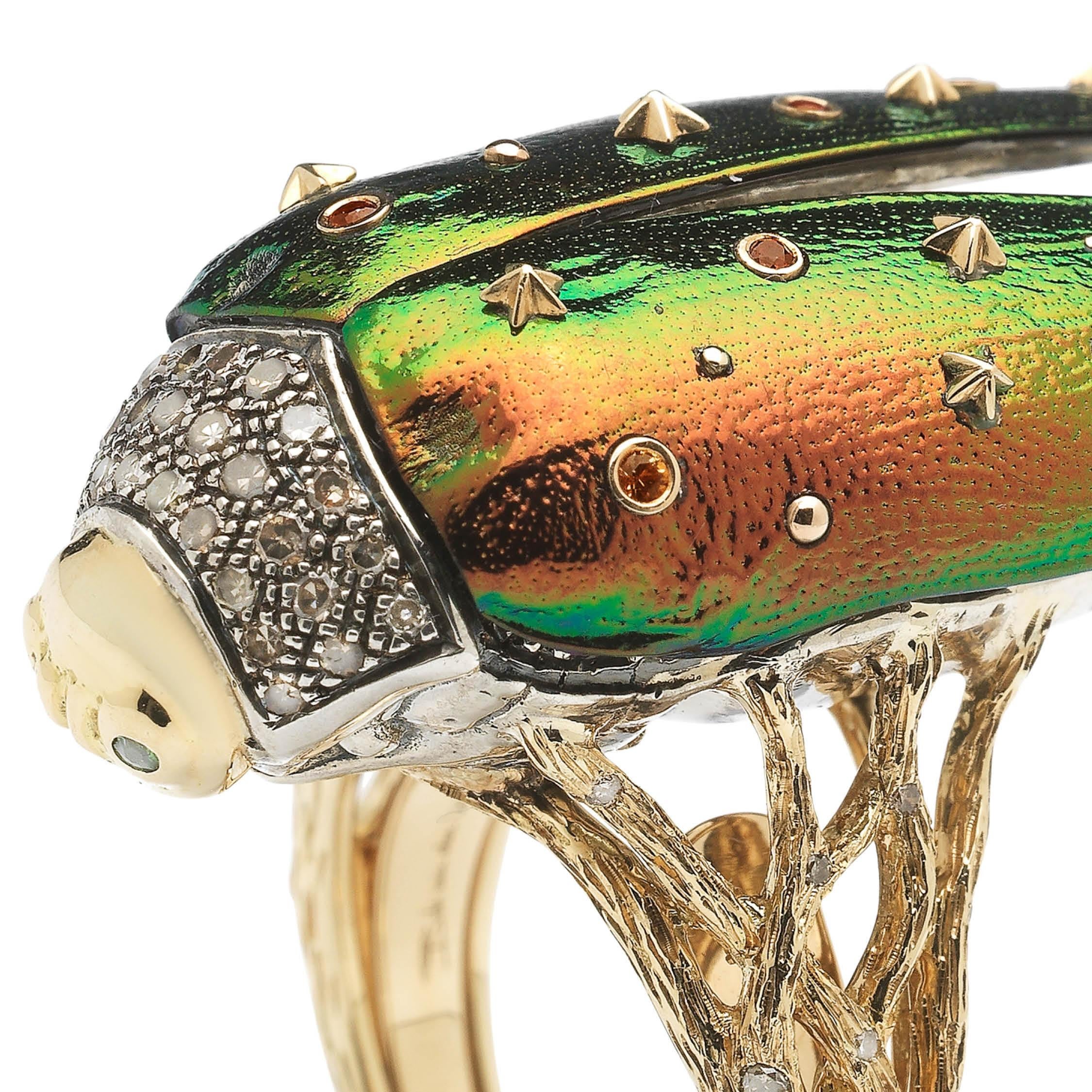 This ornate cocktail ring spotlights the beauty of real scarab wings and their natural iridescence. Designed in 18k yellow gold and sterling silver, the bold scarab beetle in this ring is embellished with white and brown diamonds and green tsavorite