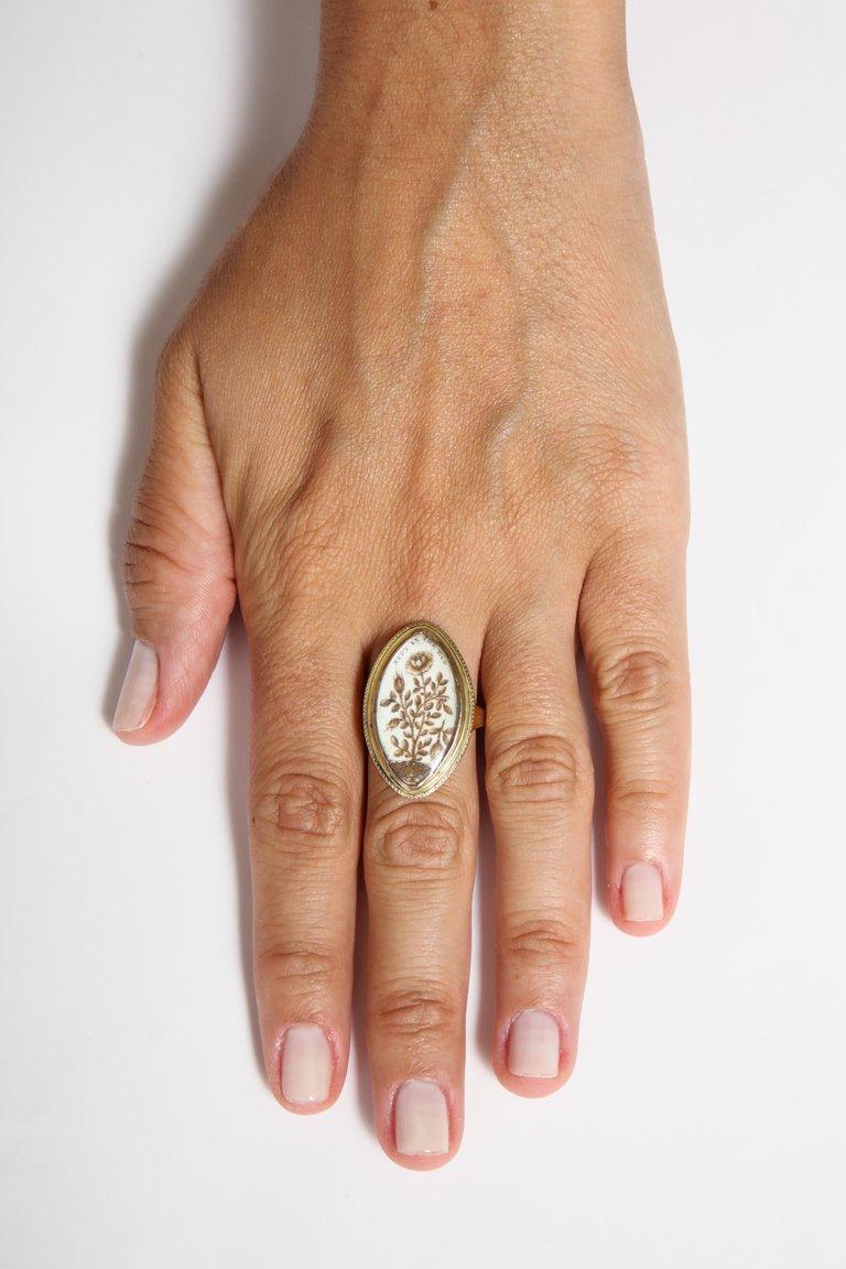 A 15 kt gold, navette shaped crystal covered ring encloses a gold rose bush with a broken bud above which is written 