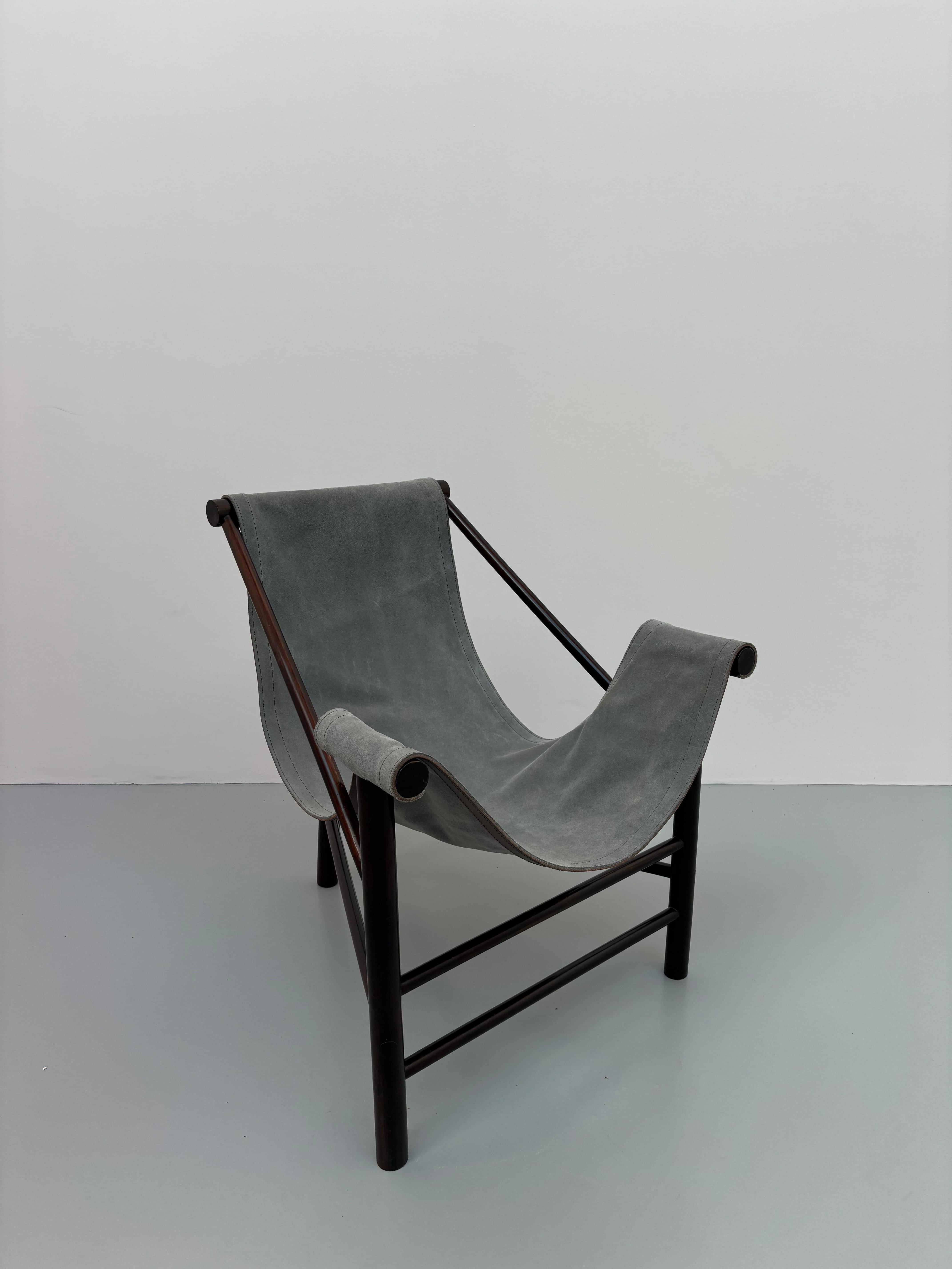 Raro Fauteuil, circa 1985, à assise et dossier en daim gris tendu et disposés sur une structure en imbuia formant les accoudoirs et reposant sur trois pieds de type rondins joints par des barreaux d'entretoise en partie basse.H. : 83,5 cm. - L. : 68