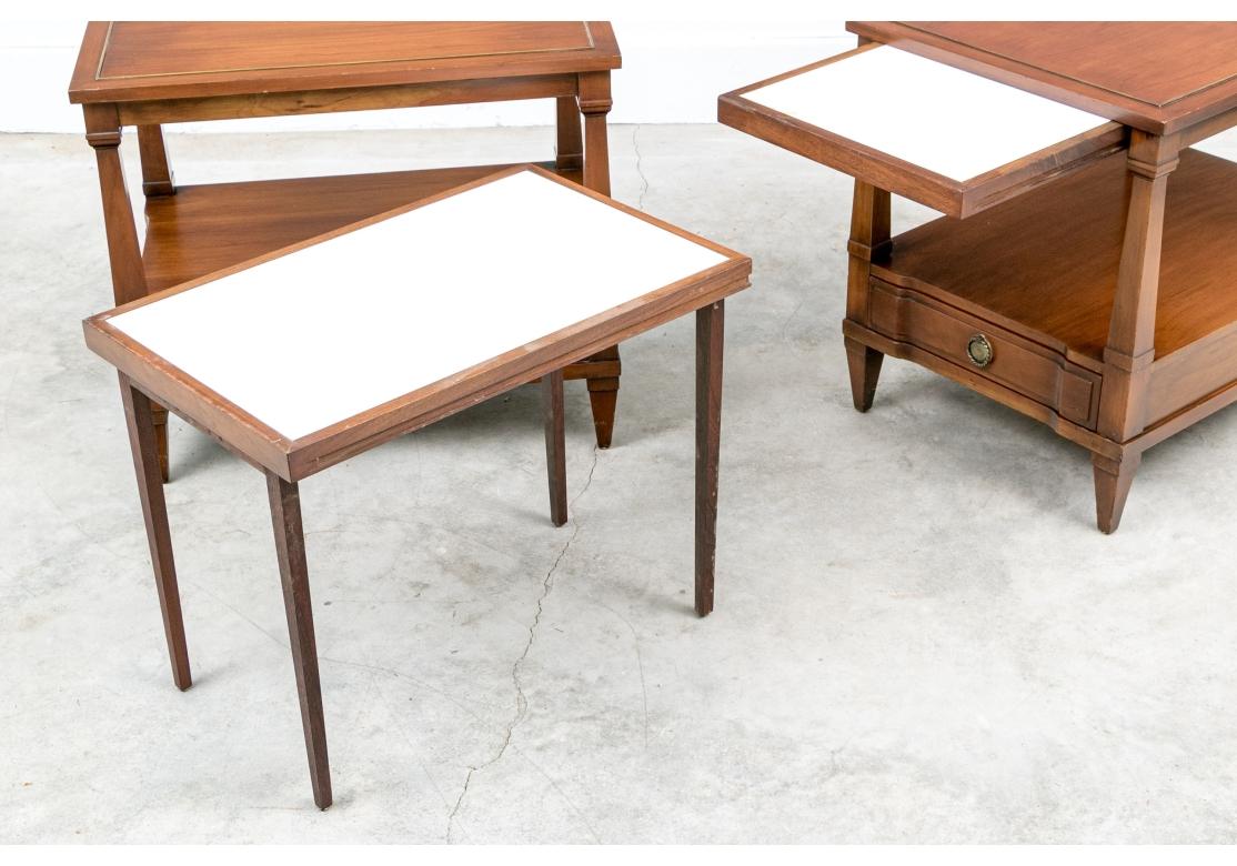 A division of John Widdicomb. Elegant tiered end tables with brass string inlaid tops, lower tiers and a drawer below with brass ring pulls. With square tapering supports and raised on square tapering legs. Along with a pair of small tables that are