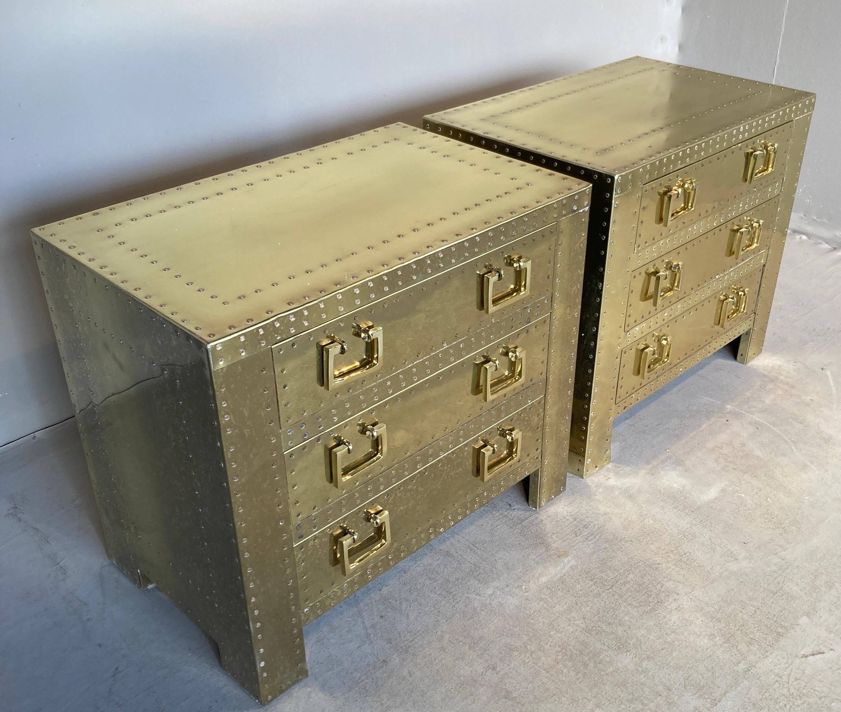Hard-to-find assembled pair of vintage 1970s brass-clad campaign style end tables in the form of chests of drawers by Sarreid Ltd. in Spain. With the customary copper tacks and chunky brasses, these tables are a decorative classic. The matching