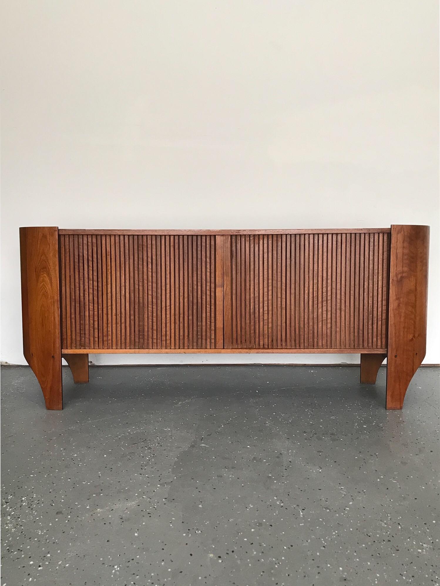 An exceptional and uncommon sculptural credenza or sideboard by Henry P. Glass. Walnut cylindrical case surrounds tambour doors. Doors open to reveal divided sections; open space on the left and right, and in the center a shelf at the top. 

Henry