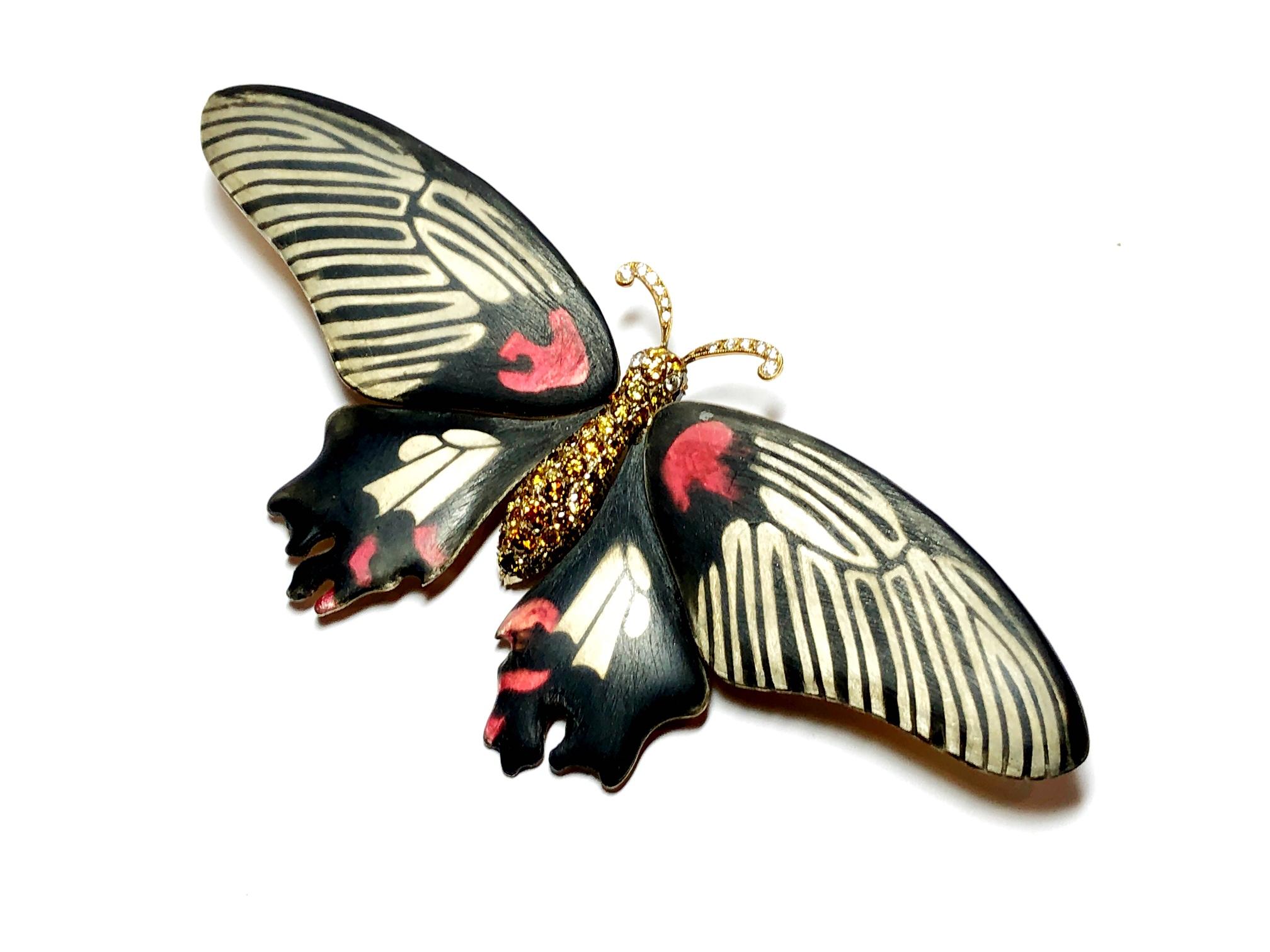 A scarlet mormon butterfly brooch, with round brilliant-cut diamond set eyes and antennae, with a yellow and brown diamond pavé set body and silver, black and red enamel wings, mounted in silver-upon-gold. The total diamond weight is approximately