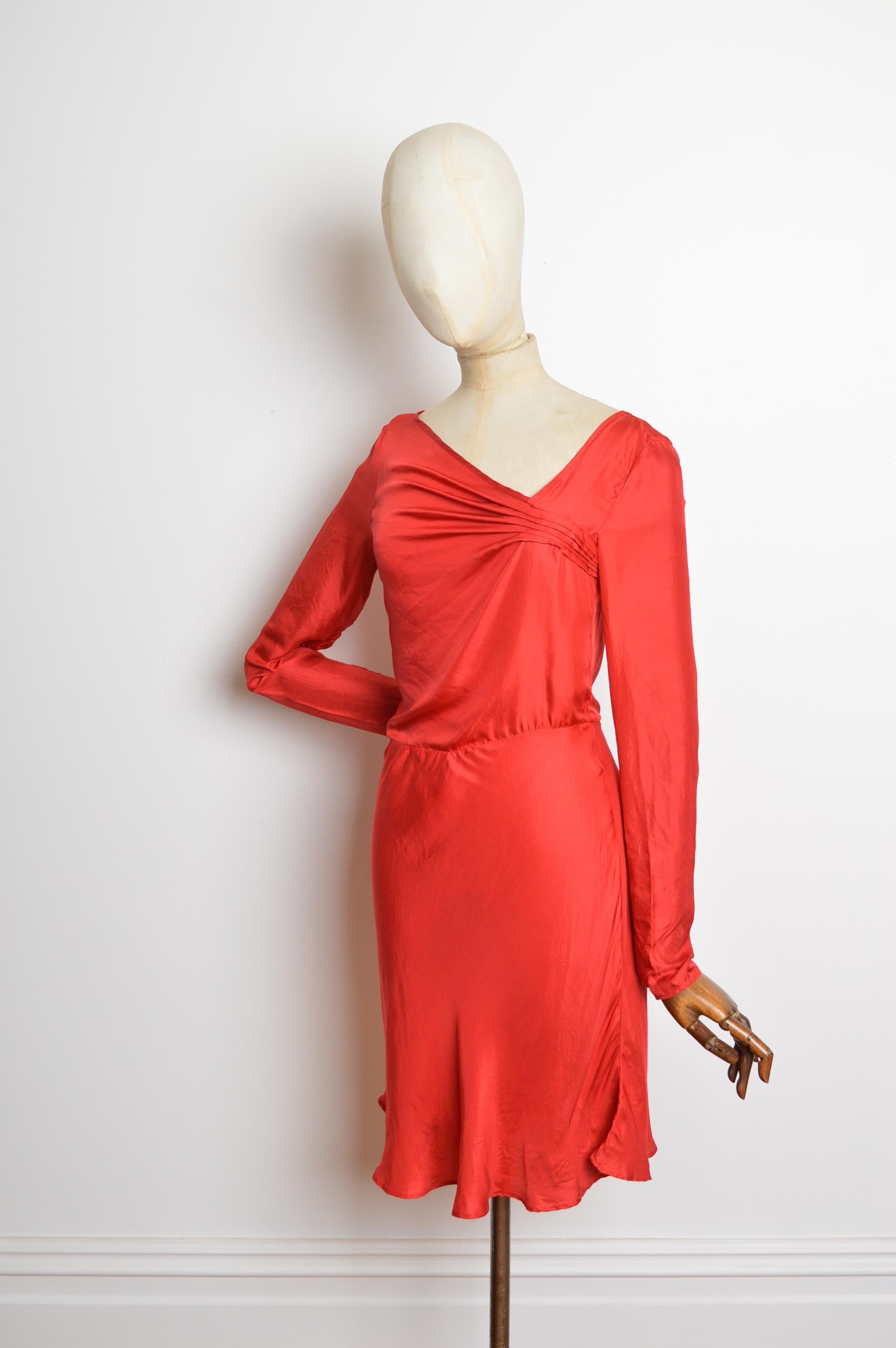 Cette magnifique robe en soie John Galliano se caractérise par un drapé en biais, un col asymétrique, des manches longues, une taille légèrement cintrée et une fermeture zippée dissimulée sur le côté. 
Les mesures sont indiquées en pouces