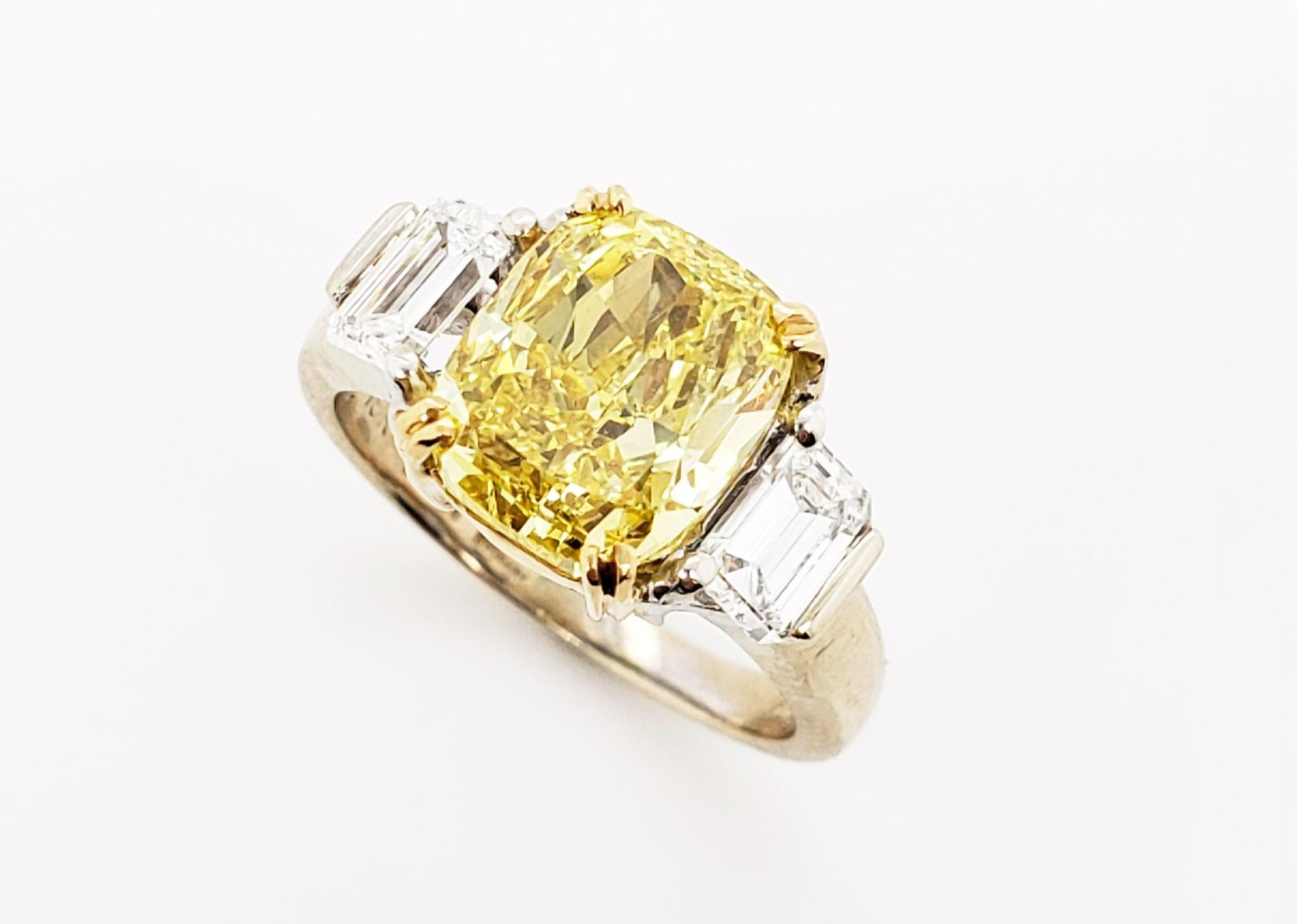 From SCARSELLI, this exceptional and rare VIVID yellow cushion diamond is VS2 clarity with a GIA grading report (see certificate picture for detailed stone information)  Flanked by a pair of small emerald cut white diamonds of G VS2 quality, this