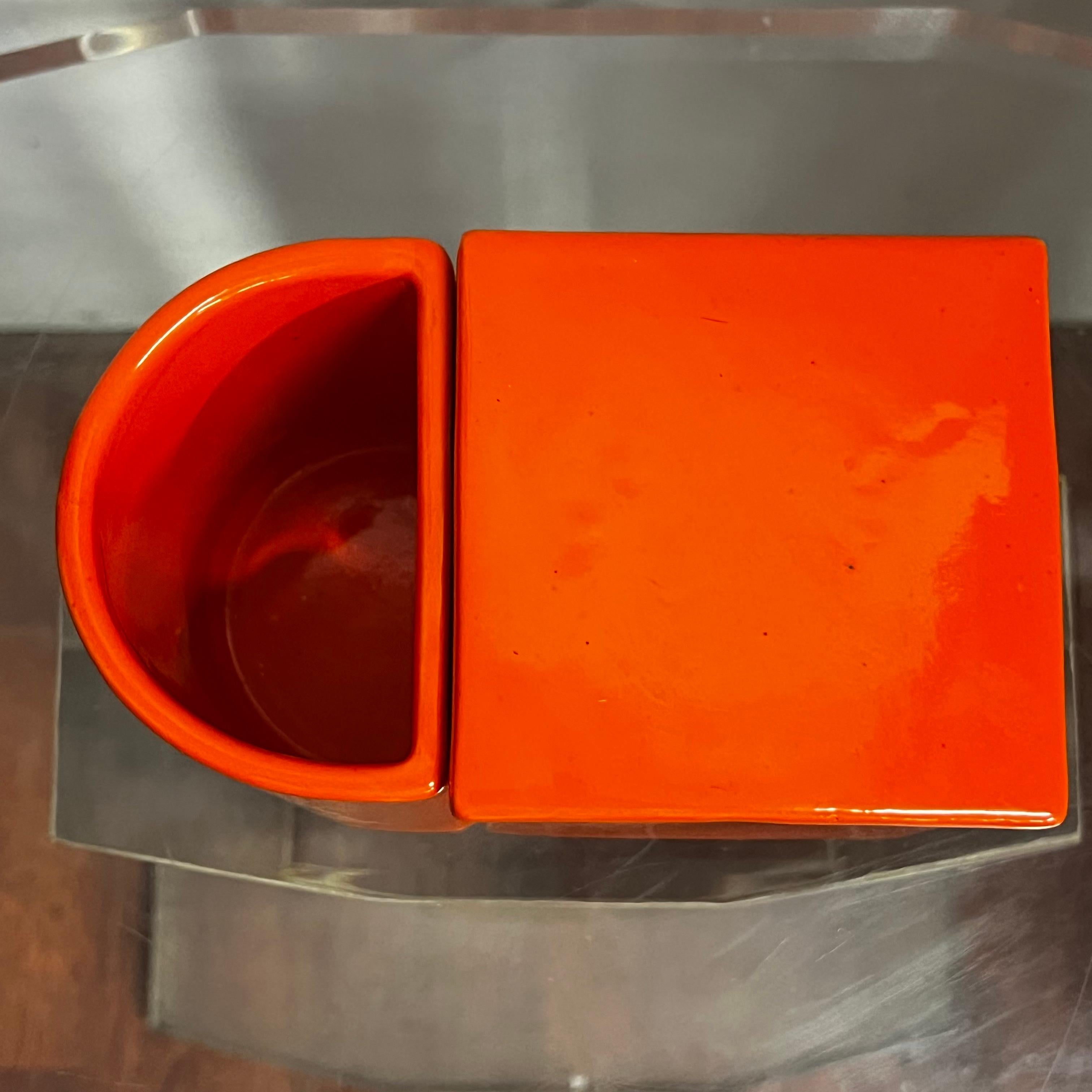 Grande scatola portaoggetti in ceramica arancione, composta da due contenitori, uno con coperchio, l'altro a mezzaluna, aperto. Prodotto da Gabbianelli.
L'oggetto può essere abbinato ad uno similare ma sviluppato con un'altezza maggiore.