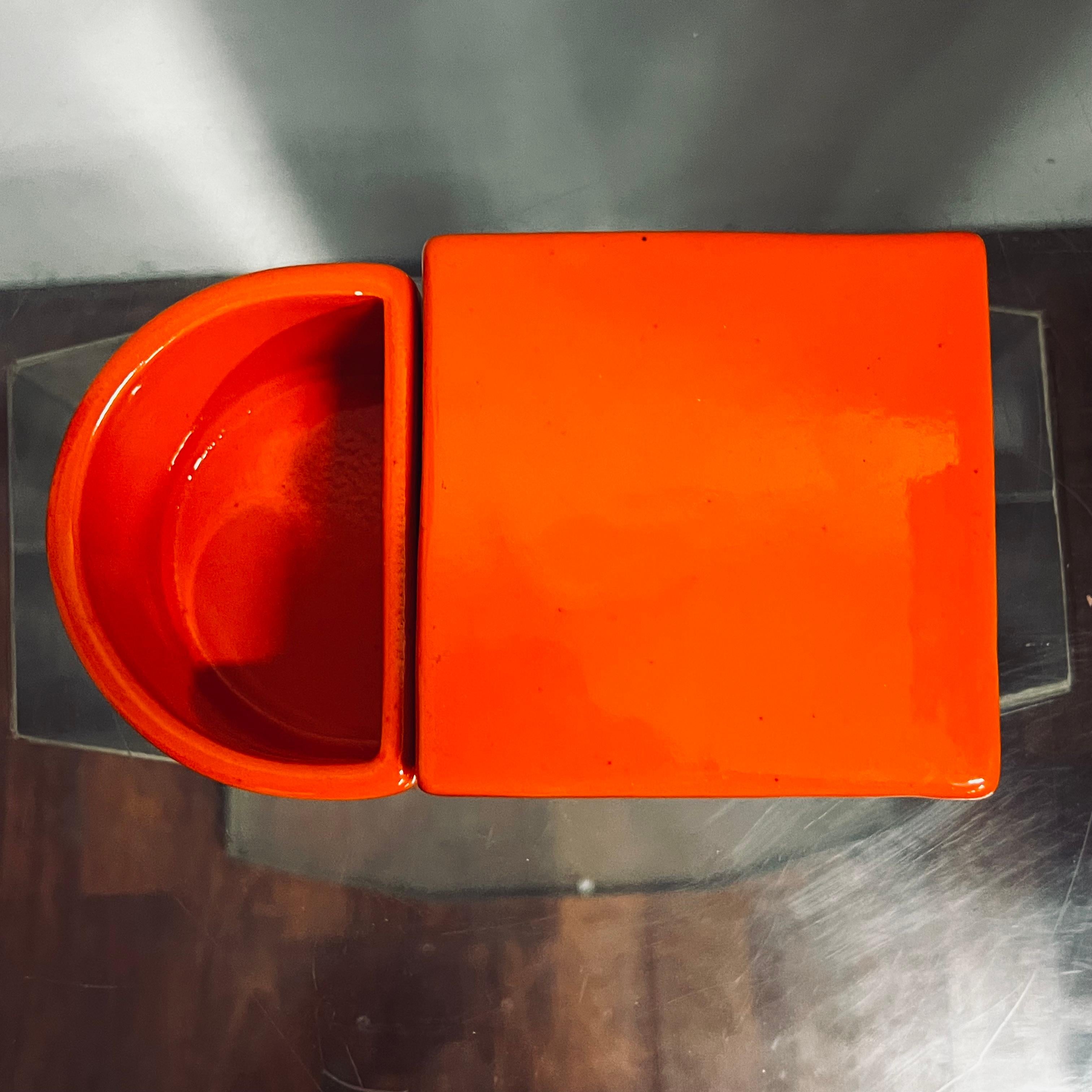 Small orange ceramic storage box, consisting of two containers, one with lid, the other crescent-shaped, open. Produced by Gabbianelli.
The object can be matched with a similar one but developed with a greater height.