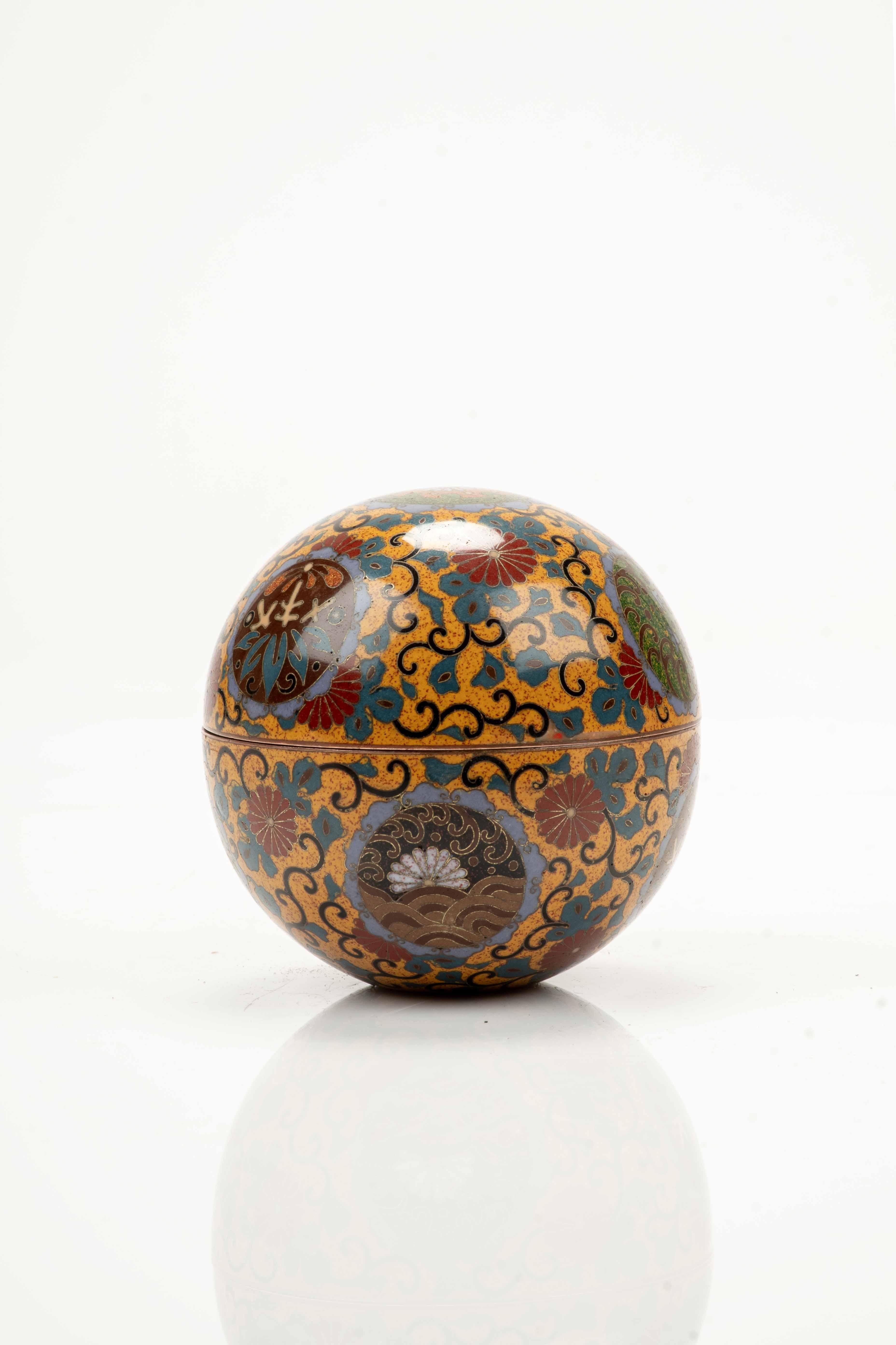 Scatola sferica kogo in smalti cloisonné decorata con motivi floreali stilizzati dai colori vivaci e riserve circolari su fondo giallo ocra. La parte superiore è impreziosita da un mon imperiale a 16 petali. 

Periodo: Meiji fine XIX