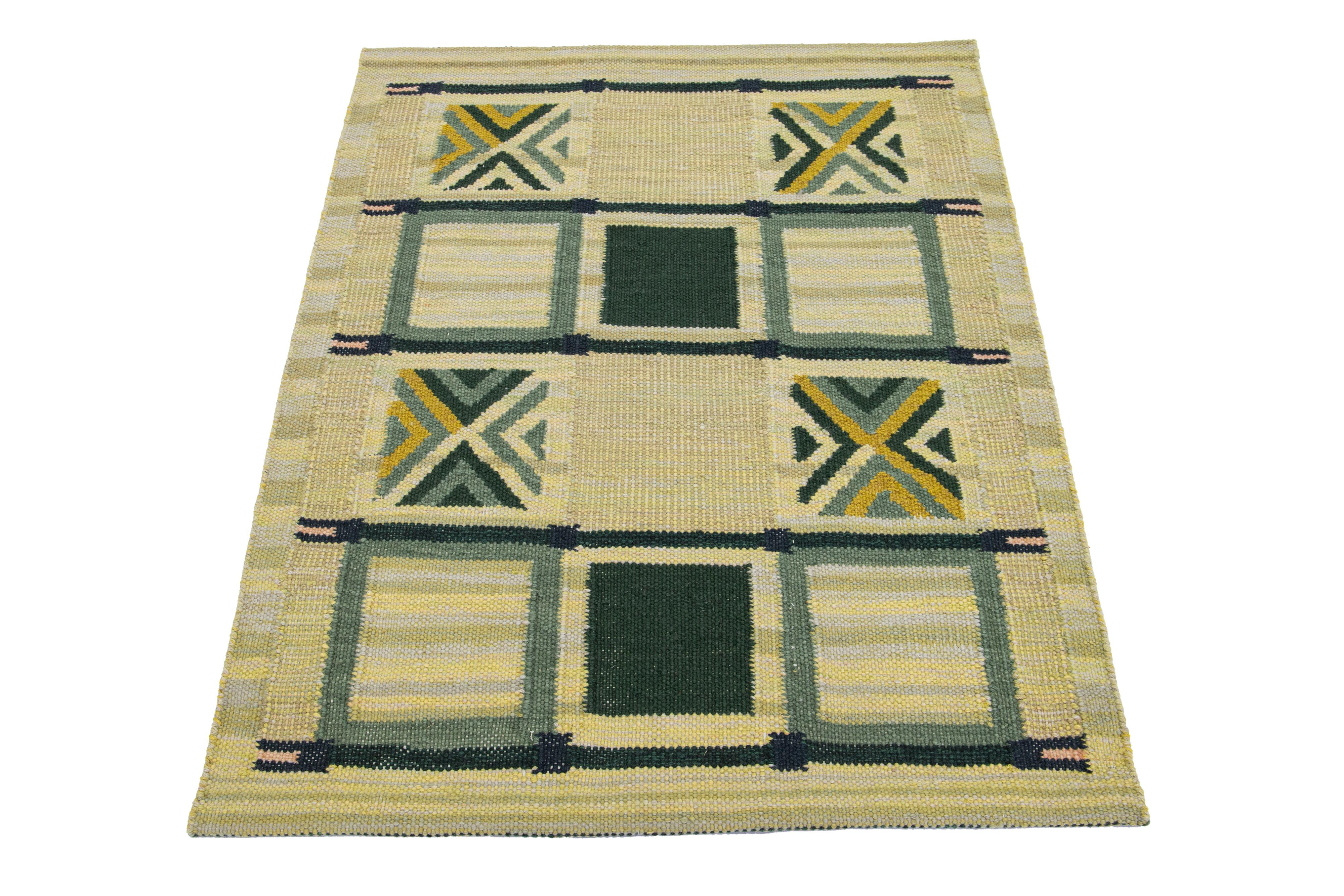 This Swedish flatweave rug showcases a contemporary Swedish design with a beige-yellow base. It's accented with green geometric patterns throughout the rug.

 This rug measures 3'11