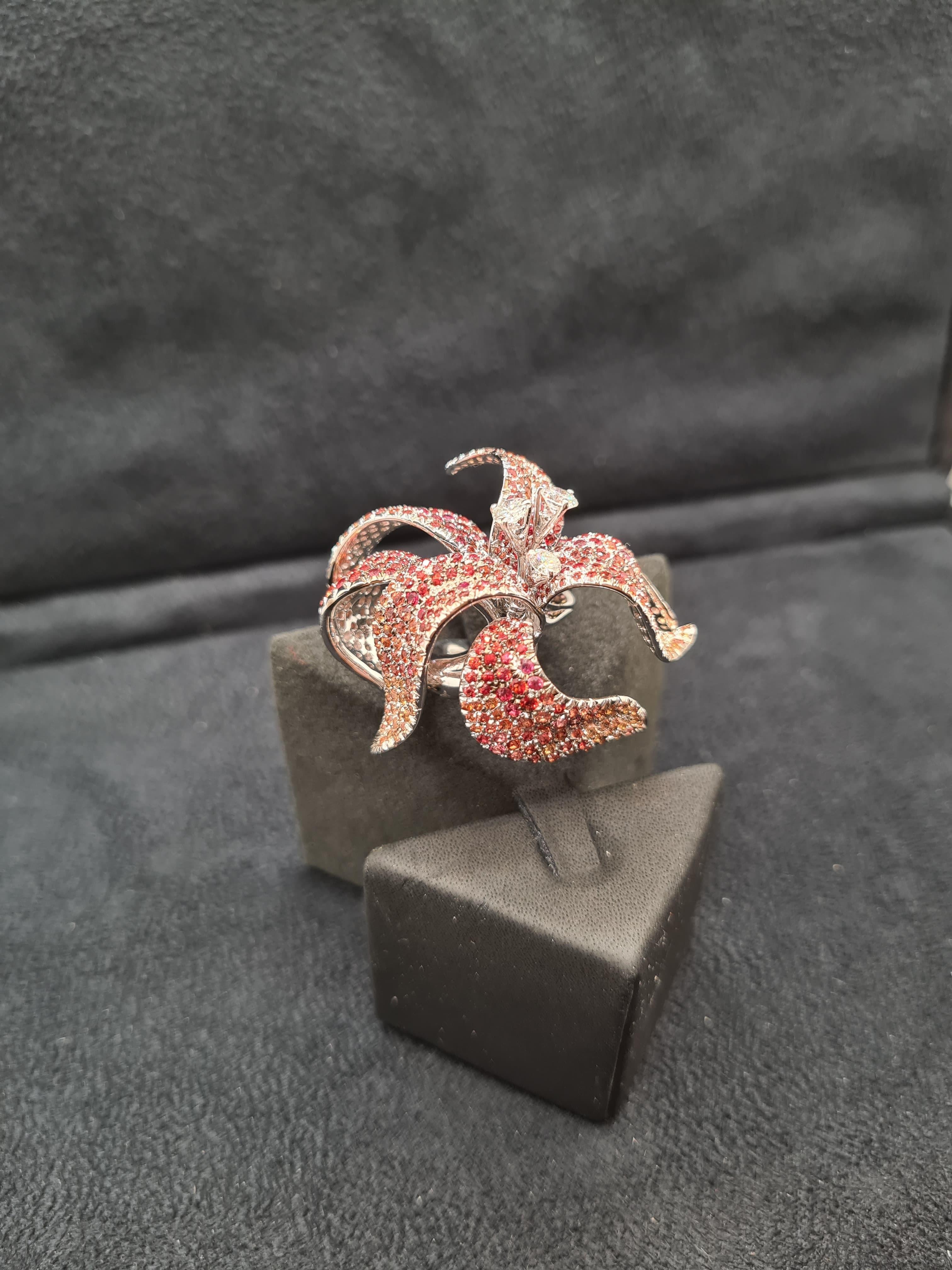 Wir stellen den faszinierenden HIBISCUS RING vor, ein schillerndes Beispiel für Eleganz und Lebendigkeit. Dieser aus Weißgold gefertigte Ring besticht durch runde Diamanten im Brillantschliff und orangefarbene Saphire, die in einem zarten