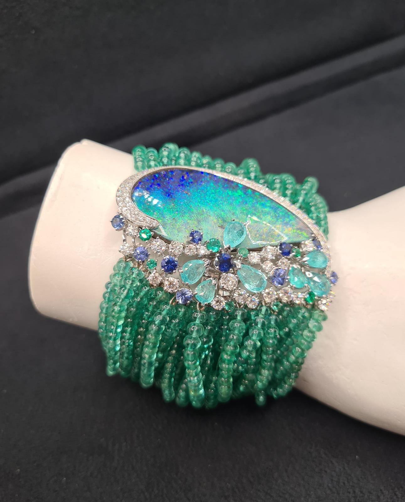 Voici le magnifique BRACELET POSEIDON EMERALD, une fusion époustouflante d'élégance et de luxe. Réalisé en or blanc, ce bracelet présente un éblouissant éventail de diamants pave, des fils d'émeraude et une opale bleue iridescente en forme de goutte