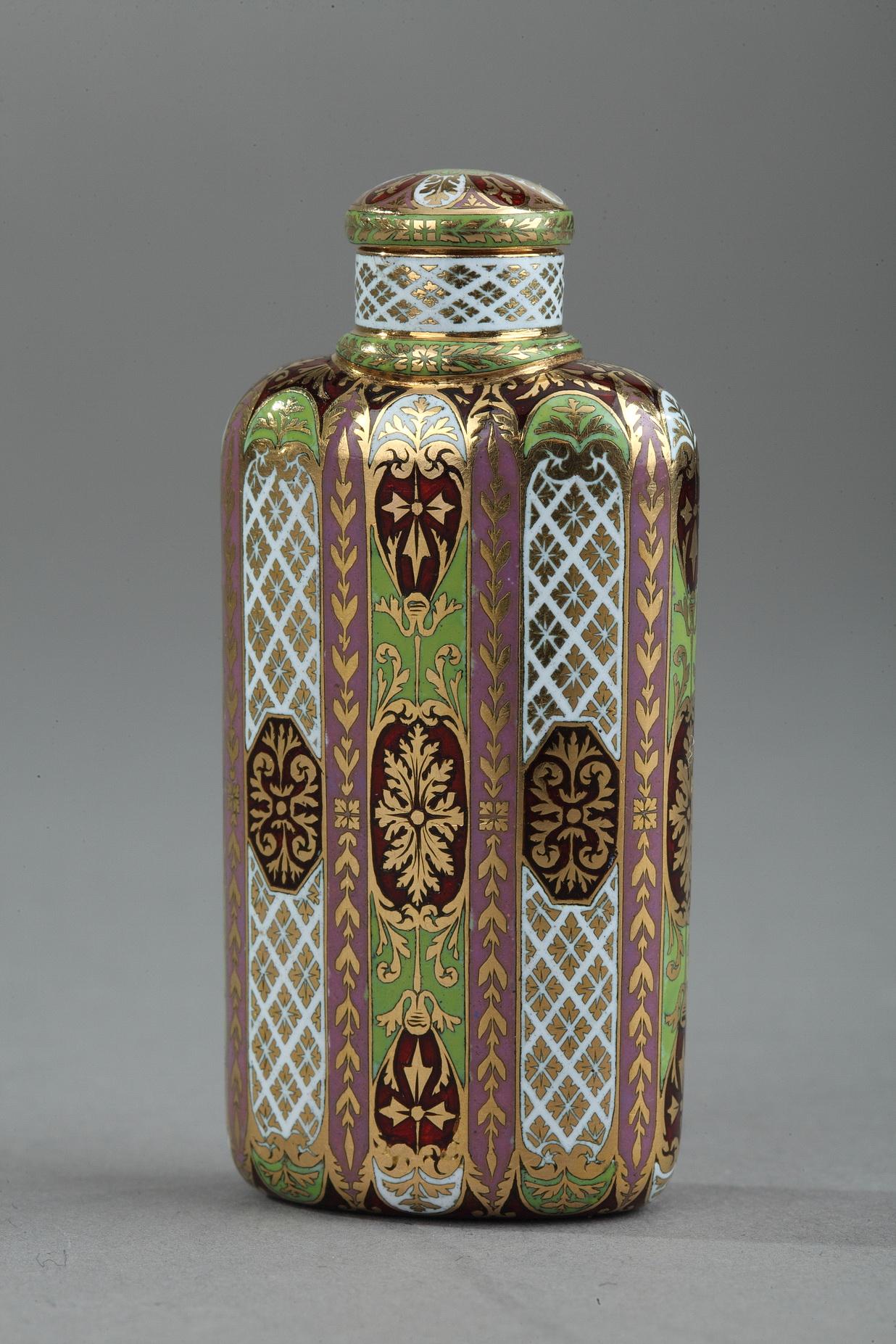 Rectangular scent perfume bottle in enameled gold. The flask features refined enameling techniques with geometric and floral patterns. The red enamel is translucent, leaving the intricate geometric pattern in the gold underneath visible. The