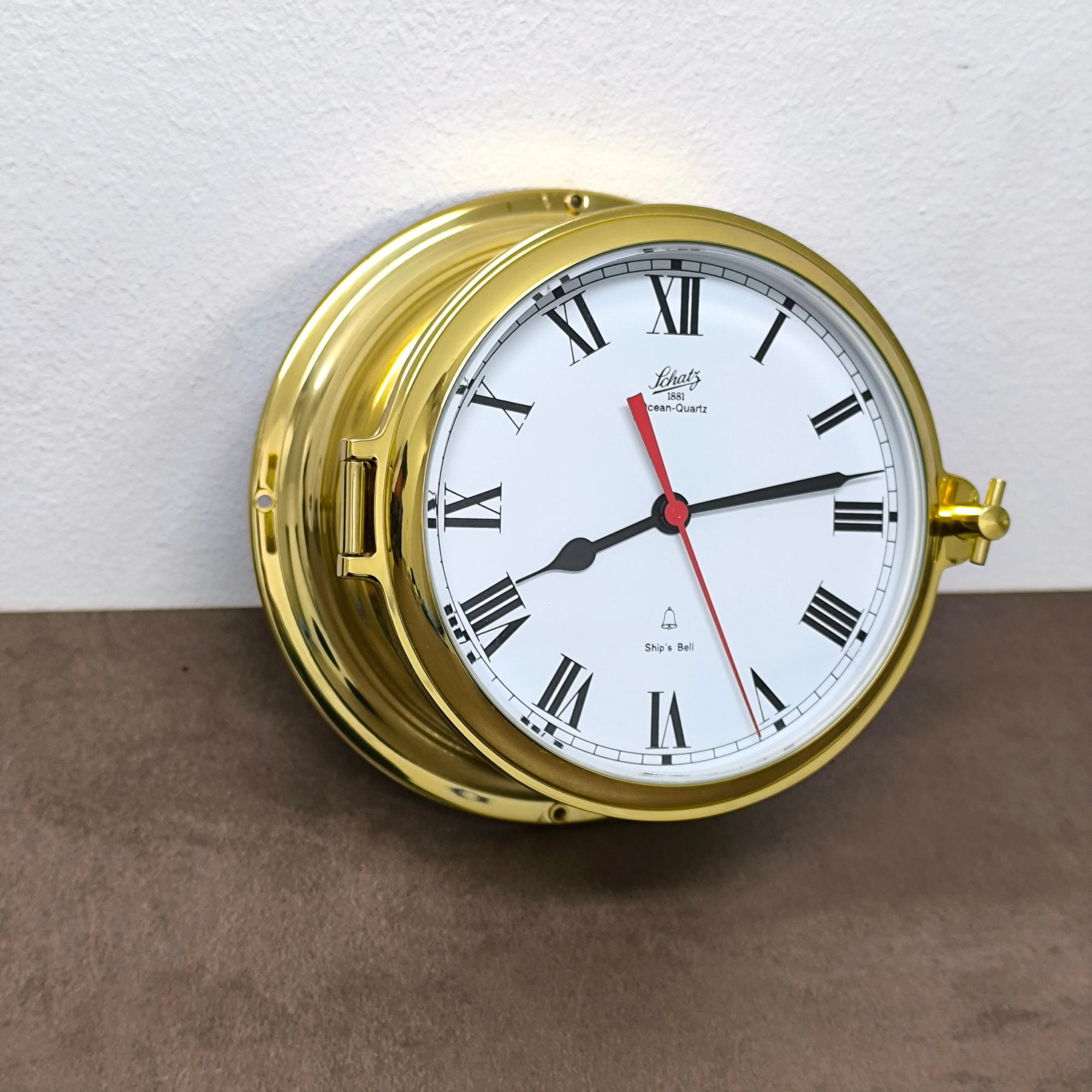 Encased in polished brass, this Schatz Ship's Bell Clock whispers the ocean's timeless song. Designed in Germany, its dial - a canvas of white - bears Roman numerals like ancient markers guiding the way, while a red second hand sweeps like a swift