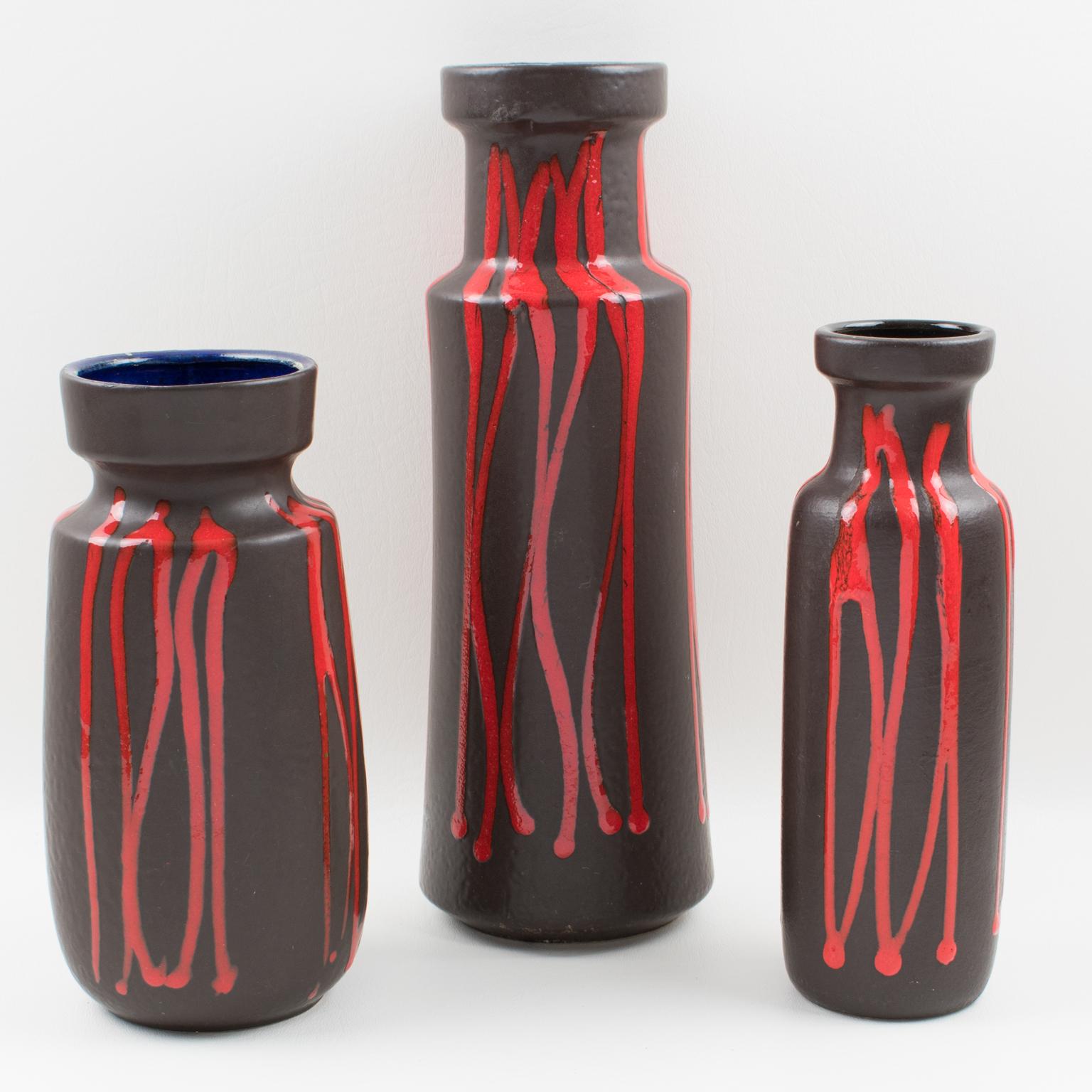 Vibrant Mid-Century Modern West Germany Scheurich Keramic set of three pottery vases in hickory black color with bright red lava glaze finish. Each vase has a specific design with strong contrasting colors and graphic patterns. Vases are all signed