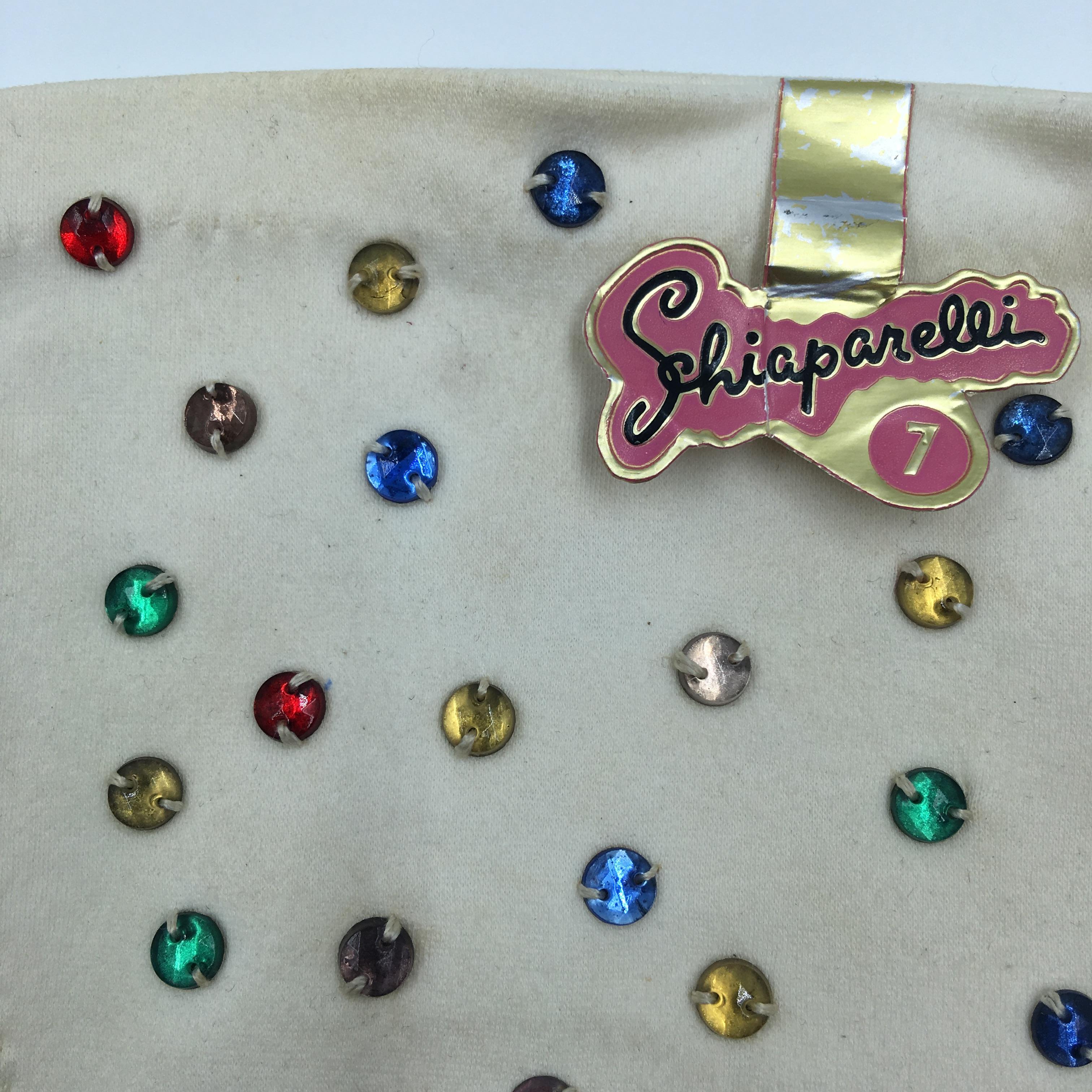 Schiaparelli, by Fownes, Cream Gloves with Hand Sewn Multi Color Beaded Rhinestones. Original paper Schiaparelli tag still on. Glove size 7. Normal vintage wear on the gloves from age and handling. See photos. 
Photo #5 shows a dark tan mark. Photo