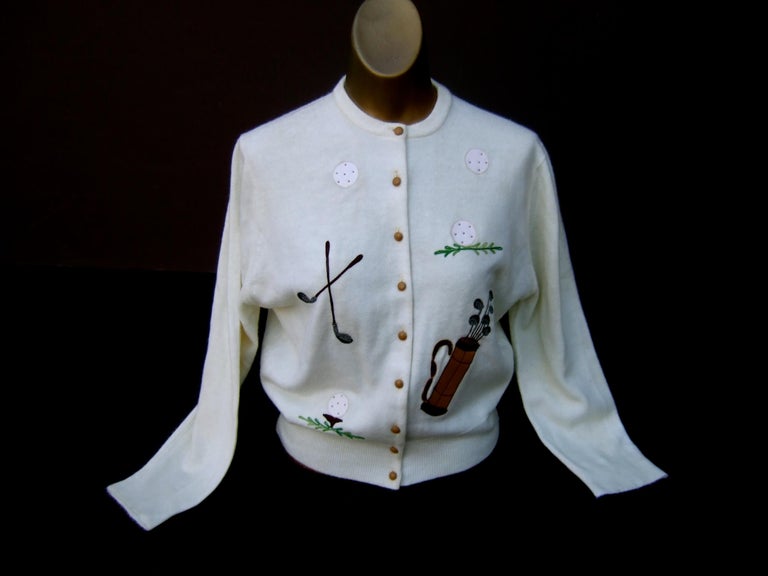 Schiaparelli Paris rare white orlon acrylic golf themed cardigan sweater c 1950s
The unique mid-century cardigan is designed with a collection of embroidered 
and vinyl applique golf accessories; a pair of embroidered golf clubs, a trio of 
white